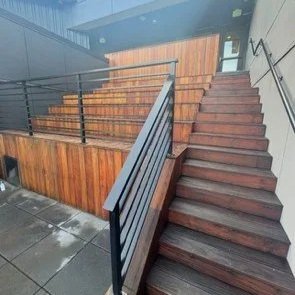 Outdoor wooden staircase with black metal railings, leading up to a building entrance.