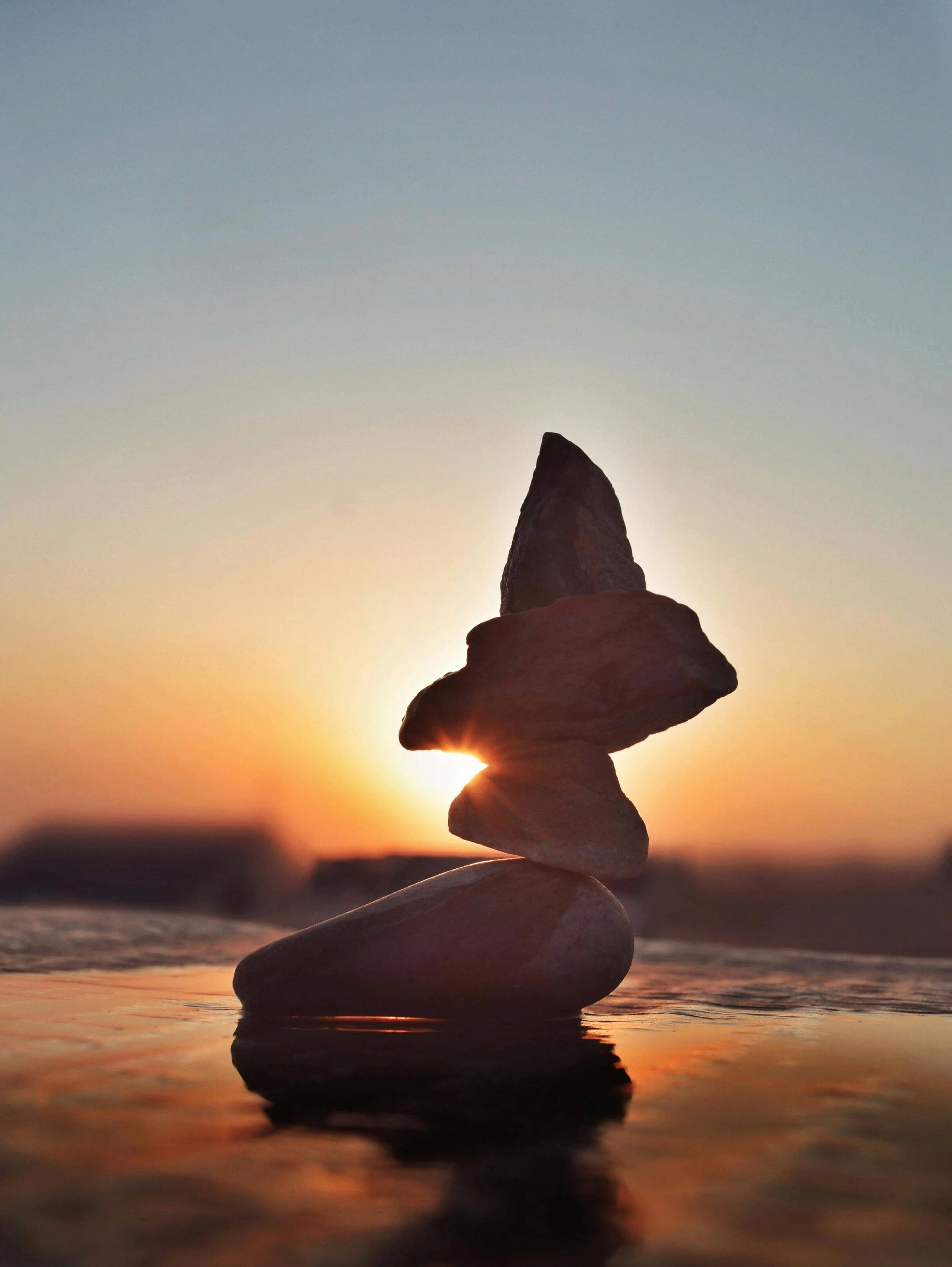 Stacked small rocks on a beach during sunset with the sun near the horizon.