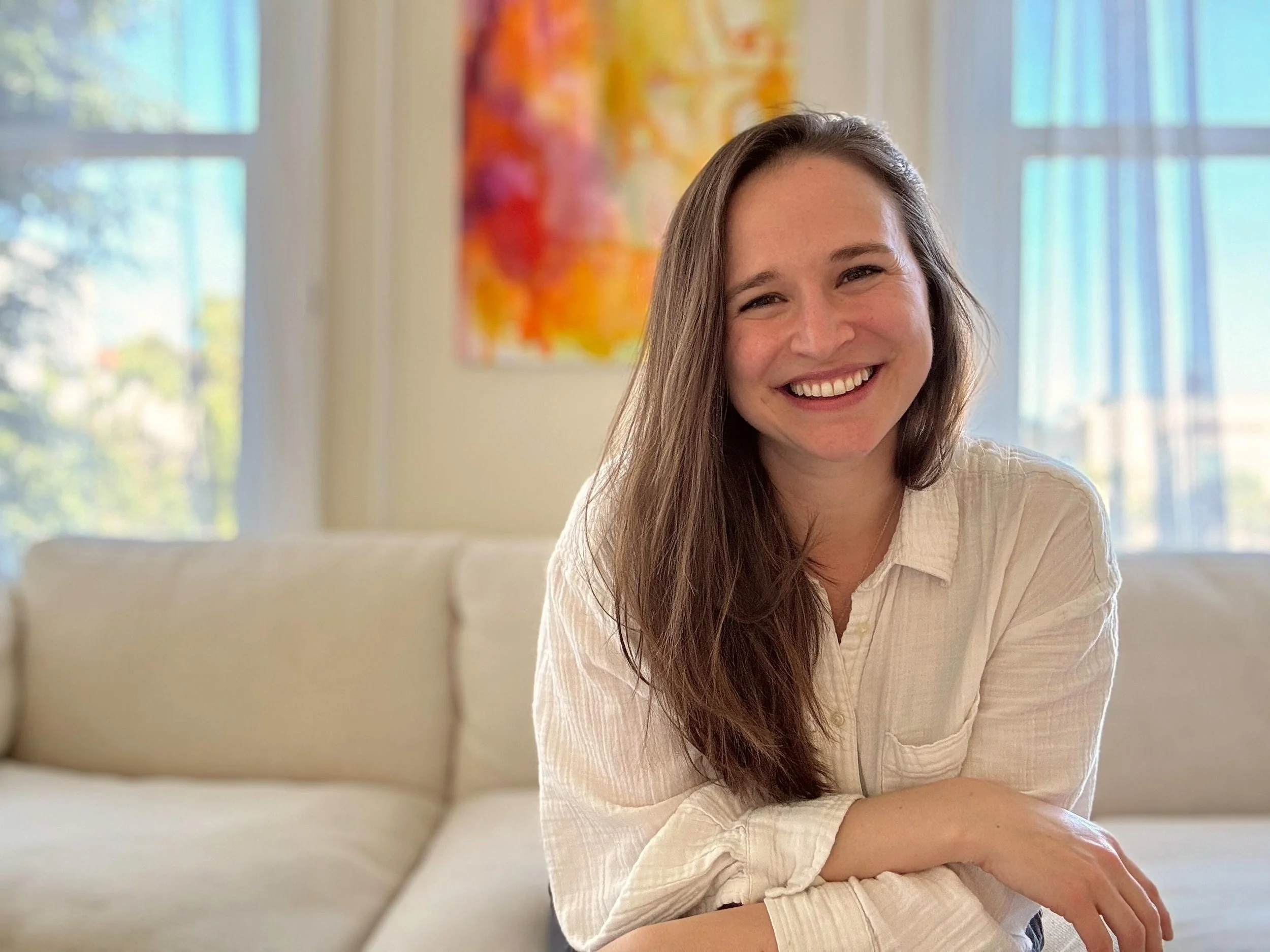 Natalie Doyle sitting on a couch smiling at the camera.