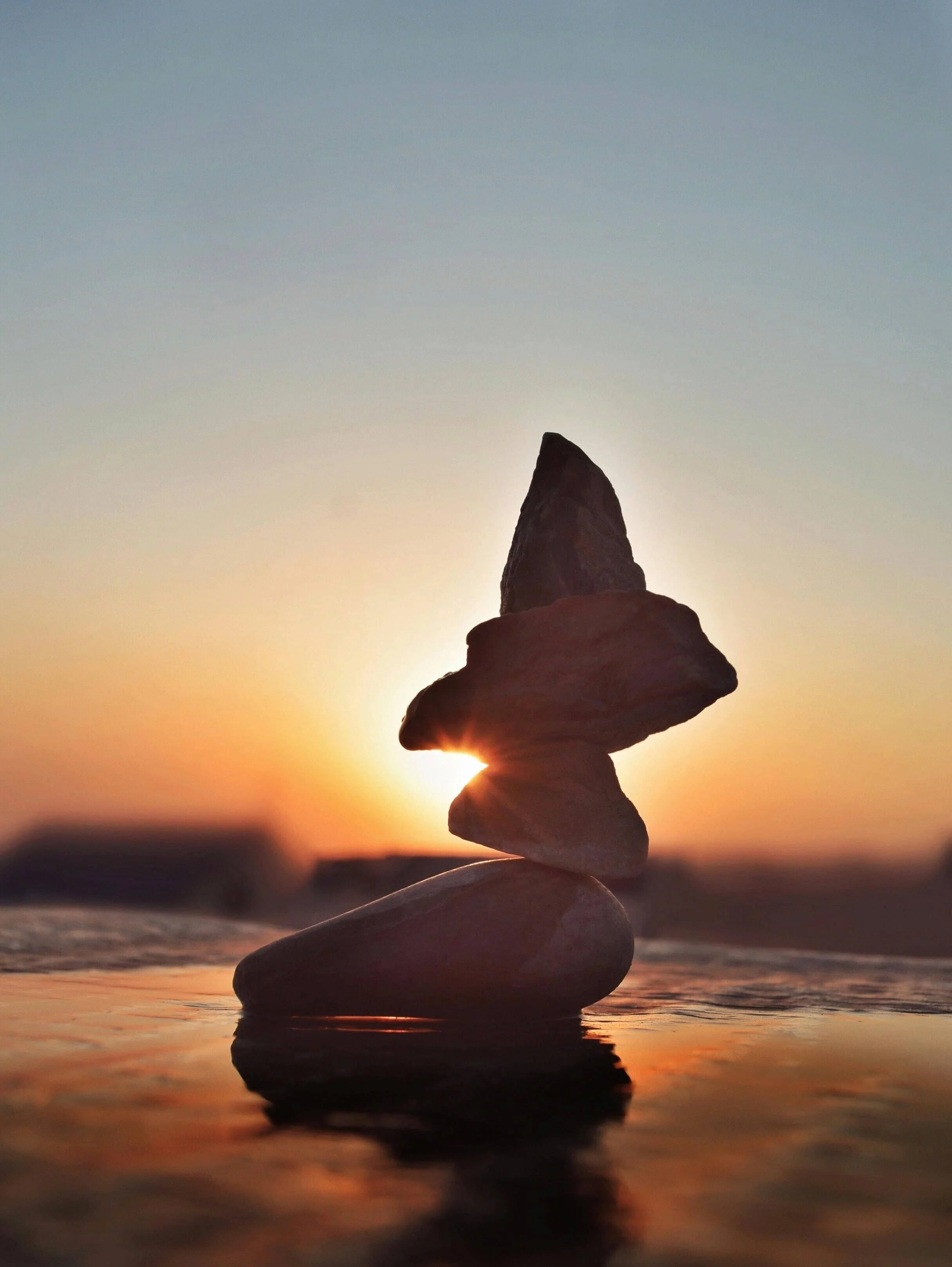 Stack of smooth stones balanced on each other on the beach during sunset.