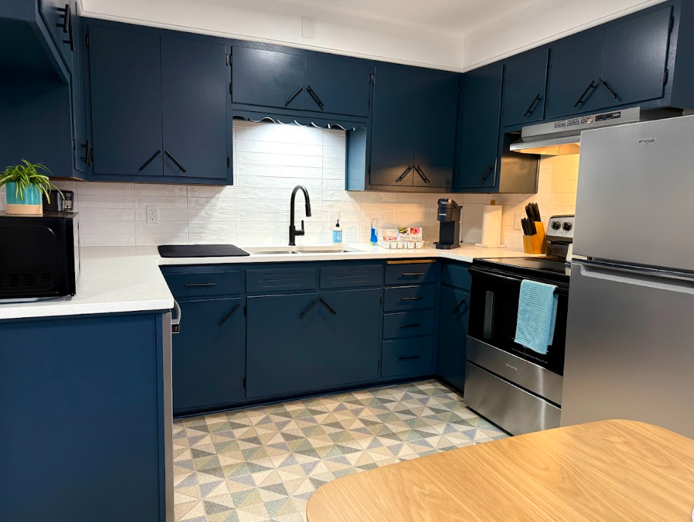 Kitchen with dark blue cabinets, white countertops, stainless steel appliances, a black microwave, a dining table, and a patterned tile floor.