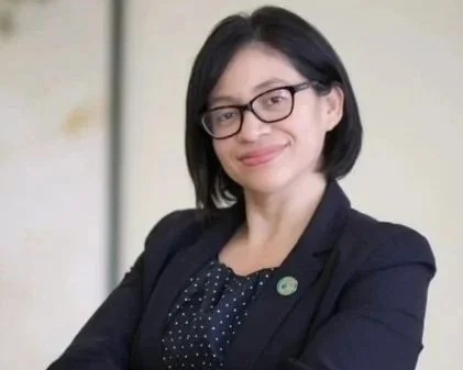 Portrait of a woman with glasses, short black hair, wearing a dark blazer and a polka dot blouse, smiling with her arms crossed.