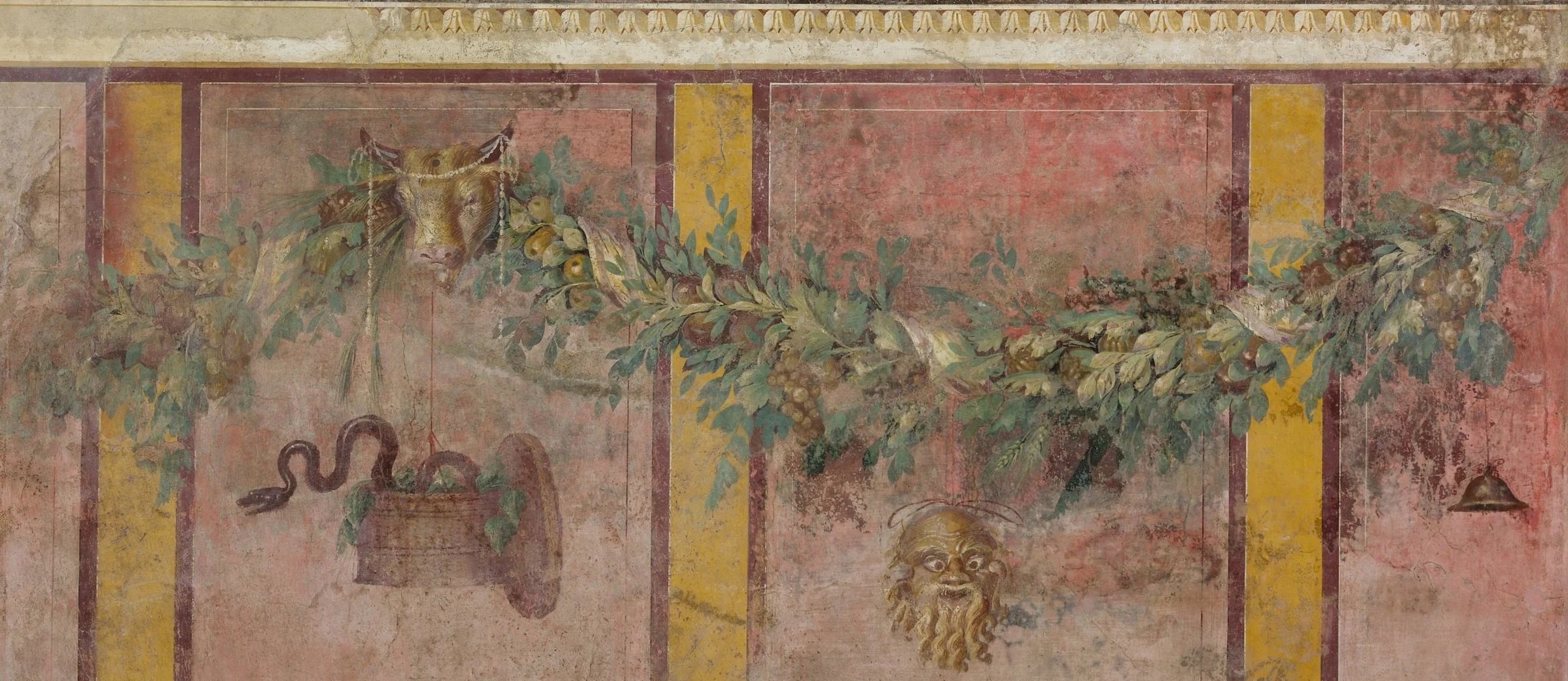 Fresco depicting a vine with grapes, a snake, and a face, on an ancient wall.