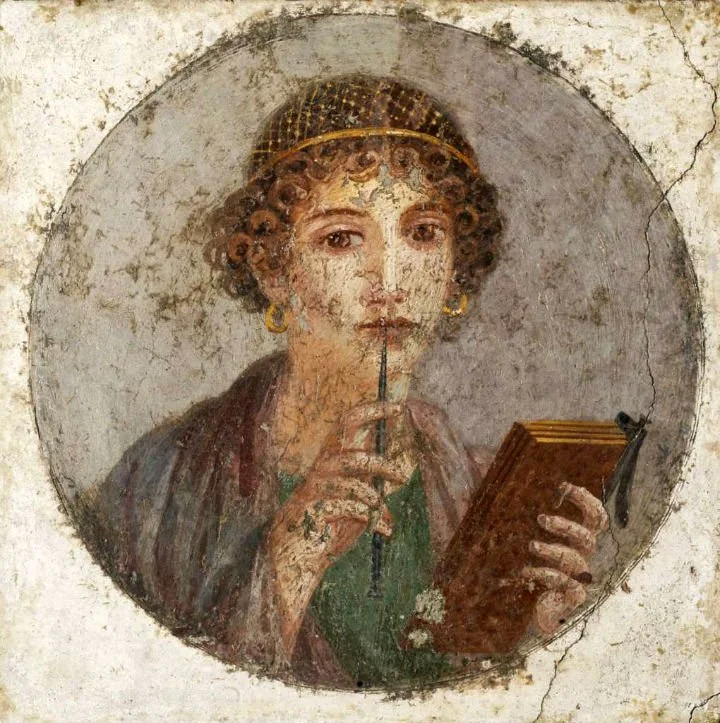 Ancient fresco of a woman with curly hair, wearing earrings, holding a stick in her mouth, and reading a book.