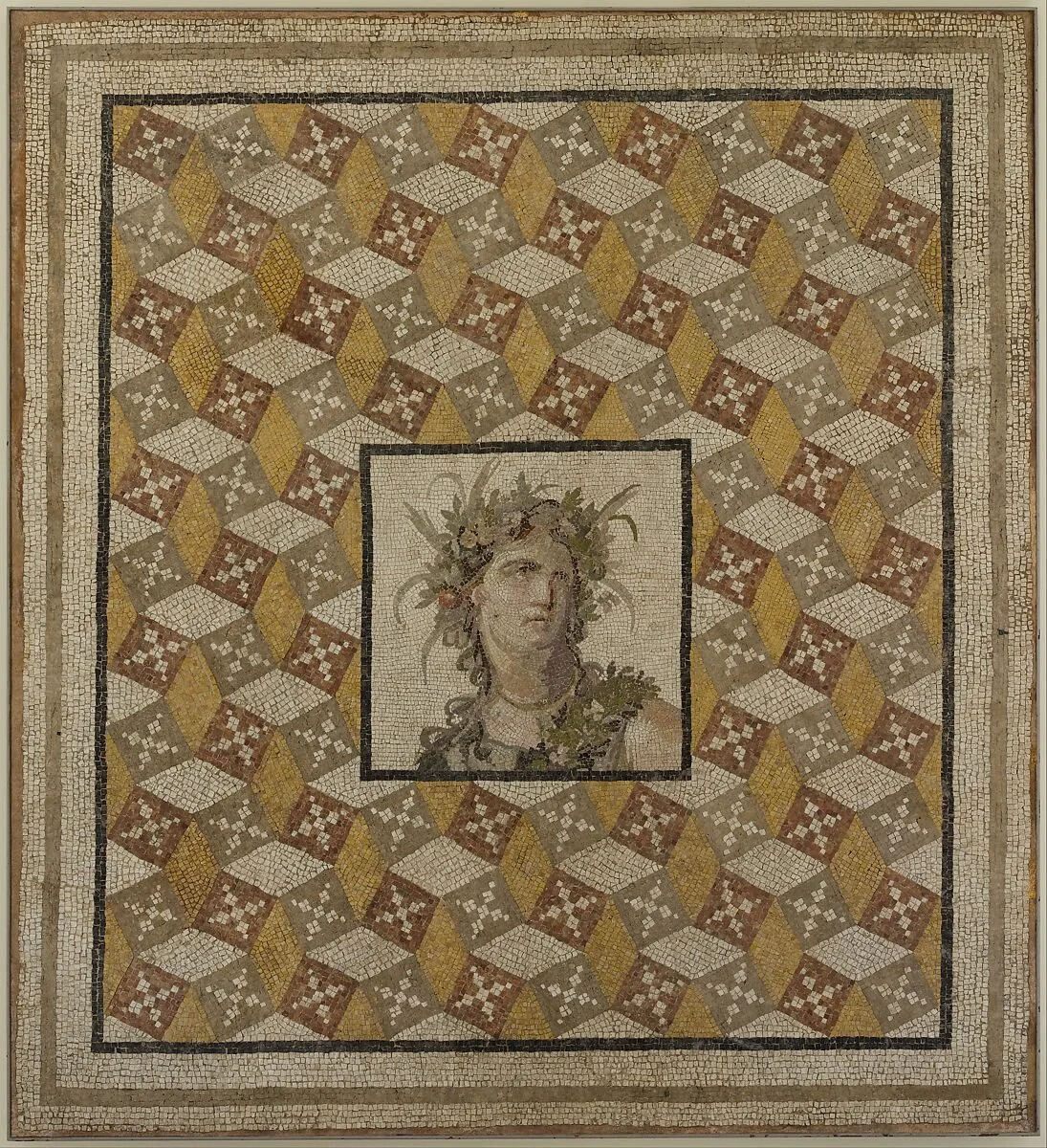 Ancient Roman mosaic artwork featuring a central portrait of a woman with leaves and branches around her head, surrounded by a geometric pattern of tiles in shades of yellow, brown, and white.
