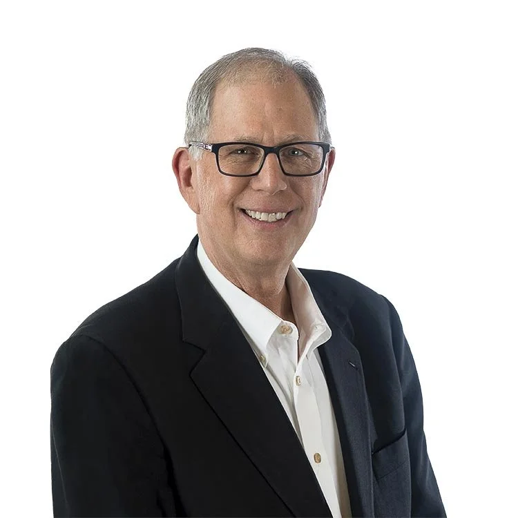 A smiling middle-aged man with gray hair, glasses, wearing a black suit jacket and white shirt against a white background.