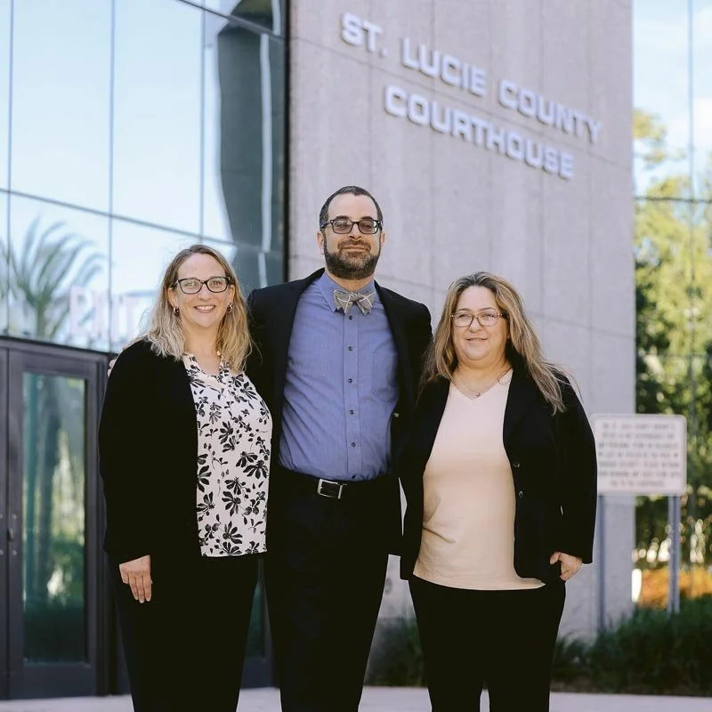 Three people standing outside St. Lucie County Courthouse, smiling for a photo.