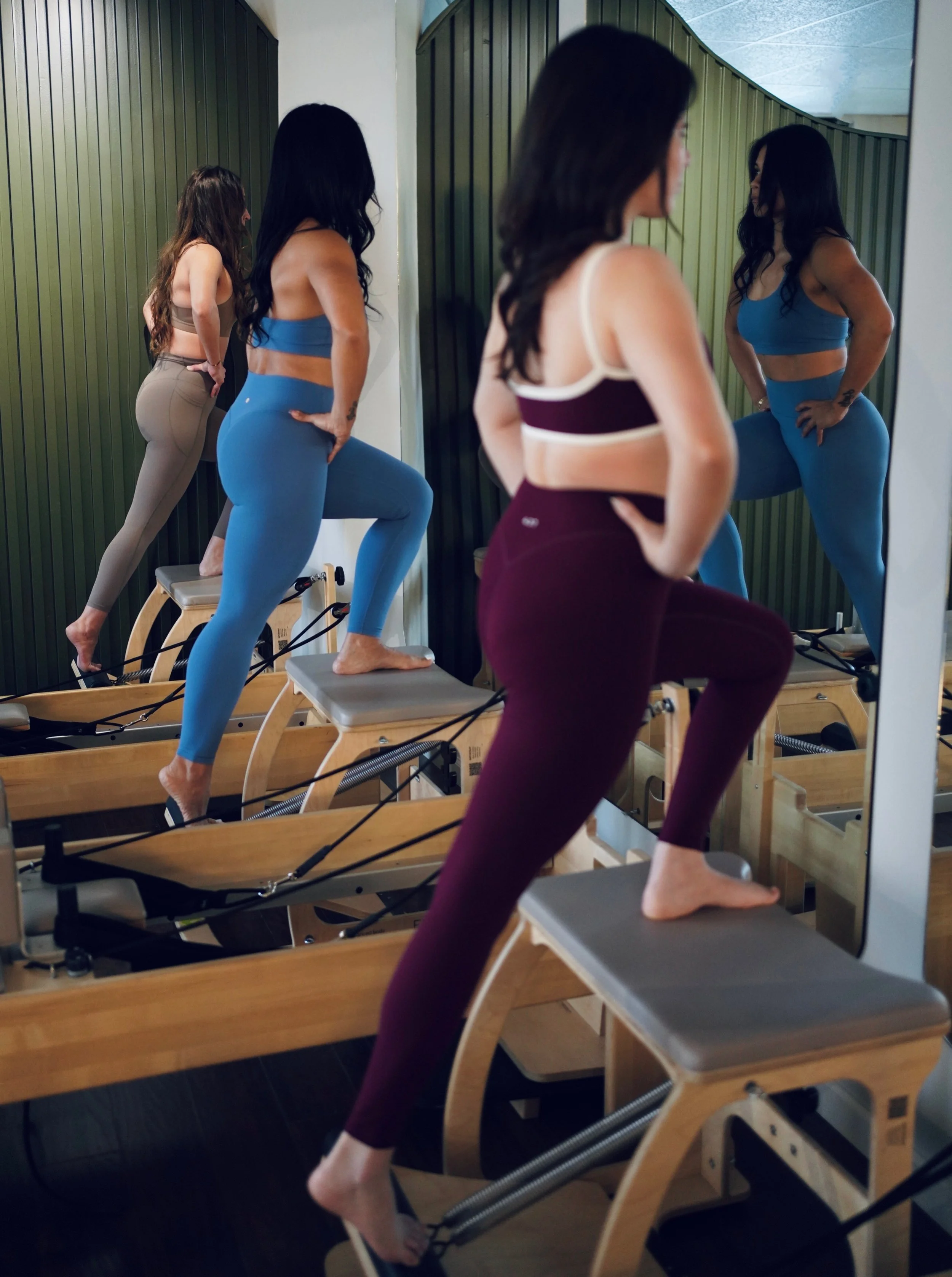 Four women practicing Pilates on reformer machines in a studio, with the women reflected in a large mirror.