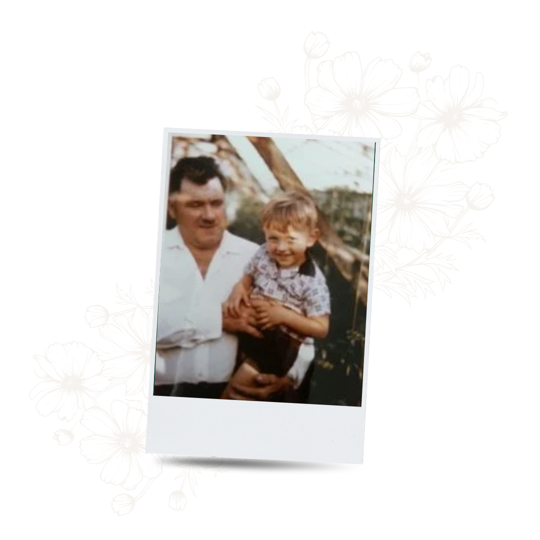 A vintage photograph of a man holding a young boy outdoors, with trees and greenery in the background.