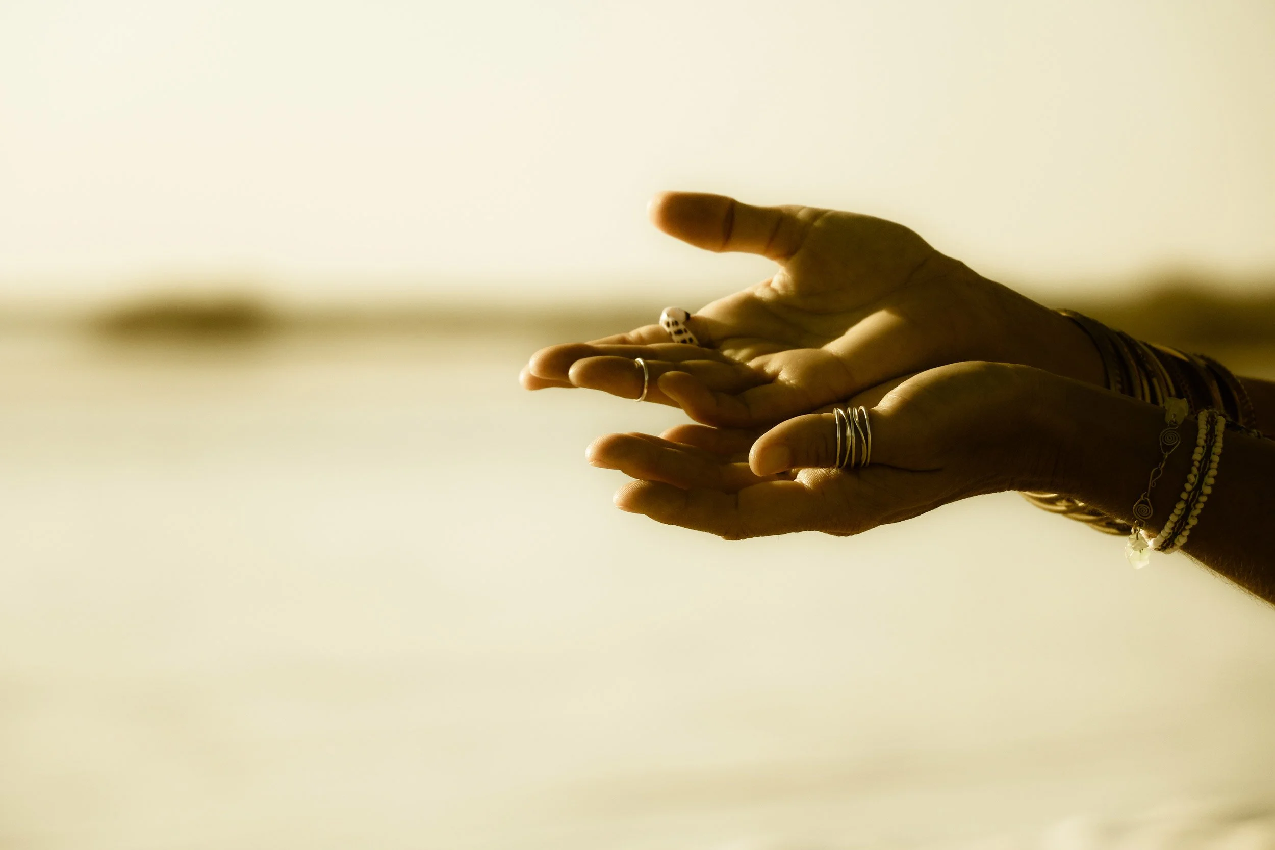 Atmosphärisches Bild offener Hände mit Fingerschmuck – vor weichgezeichnetem Hintergrund.