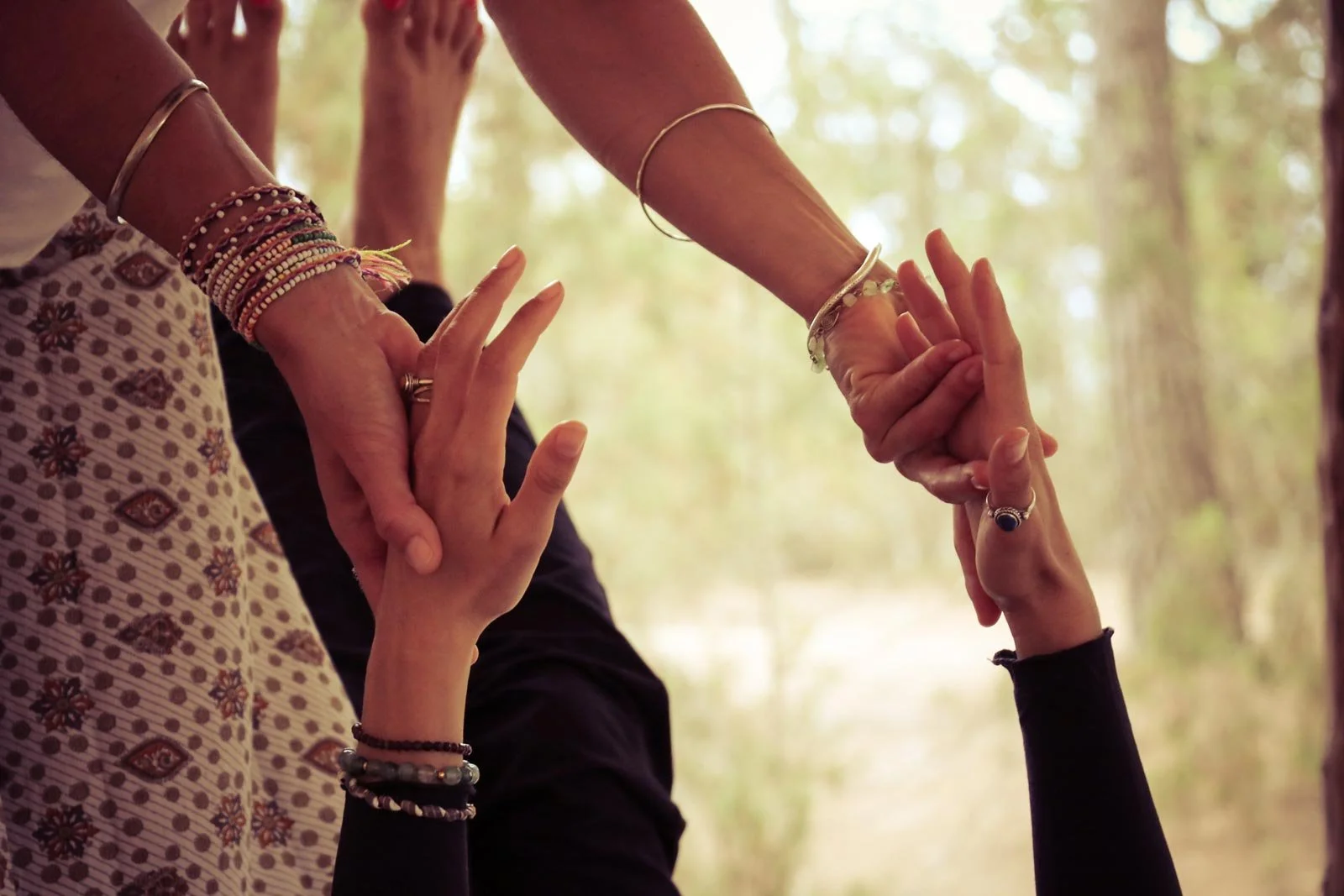 Nahaufnahme von mehreren Händen mit bunten Armbändern, die sich im Rahmen einer Yin Yoga Stunde berühren.