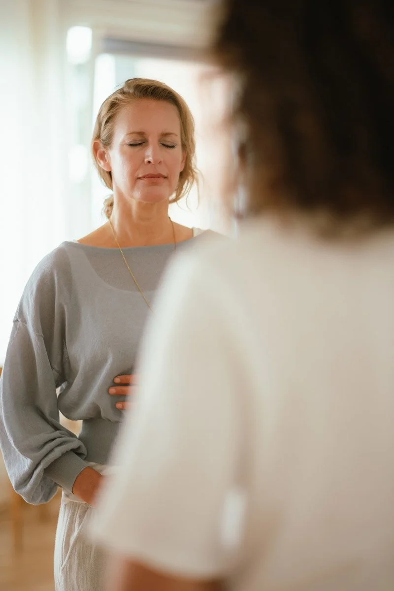 Saskia Schreiber in einer Sitzung mit Nina zur therapeutischen Einzelbegleitung. Sie stehen mit geschlossenen Augen voreinander und atmen bewusst mit den Händen auf dem Bauch.