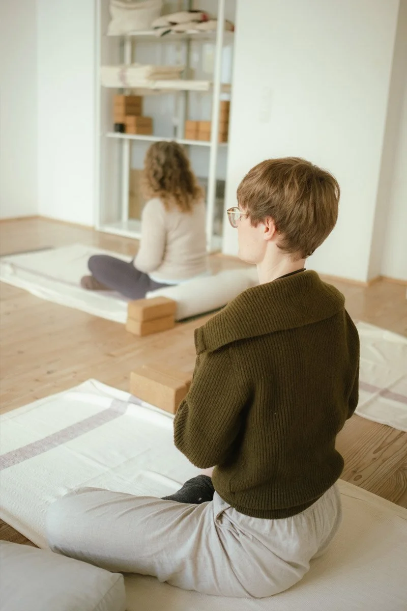 Zwei Frauen in meditativer Haltung in einem schönen, hellen Yogaraum.