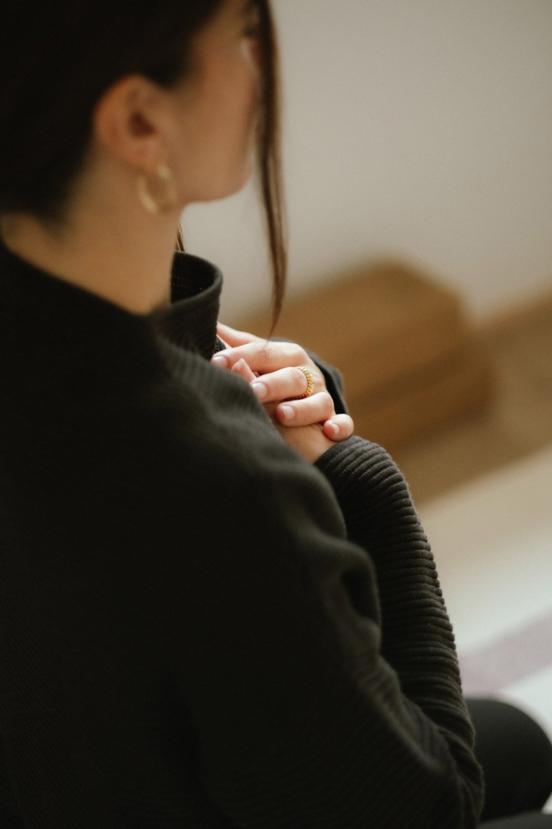 Detailaufnahme einer Schülerin von Saskia in dunkler Kleidung in meditativer Haltung mit den Händen aufs Herz gelegt.