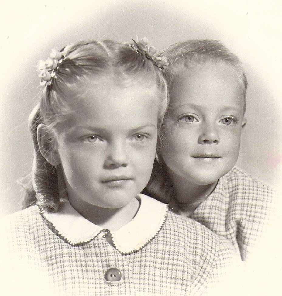 Black and white portrait of two young children, a girl with braids and a boy, both dressed in checked clothing, looking at the camera.