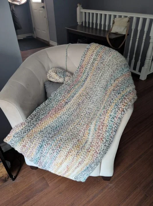 A cozy armchair with a multicolored, stitched blanket draped over it, situated in a room with dark wood floors.