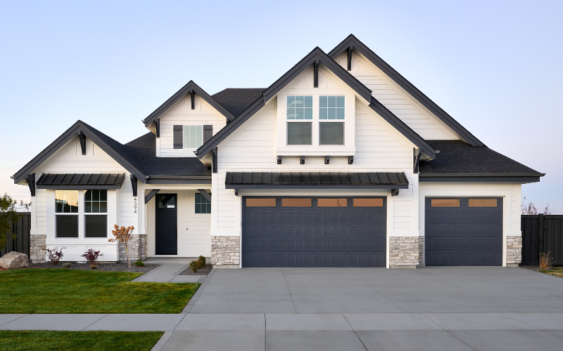Front view of a modern house with white siding, black roof, and black garage doors, surrounded by a well-maintained lawn and a concrete driveway.