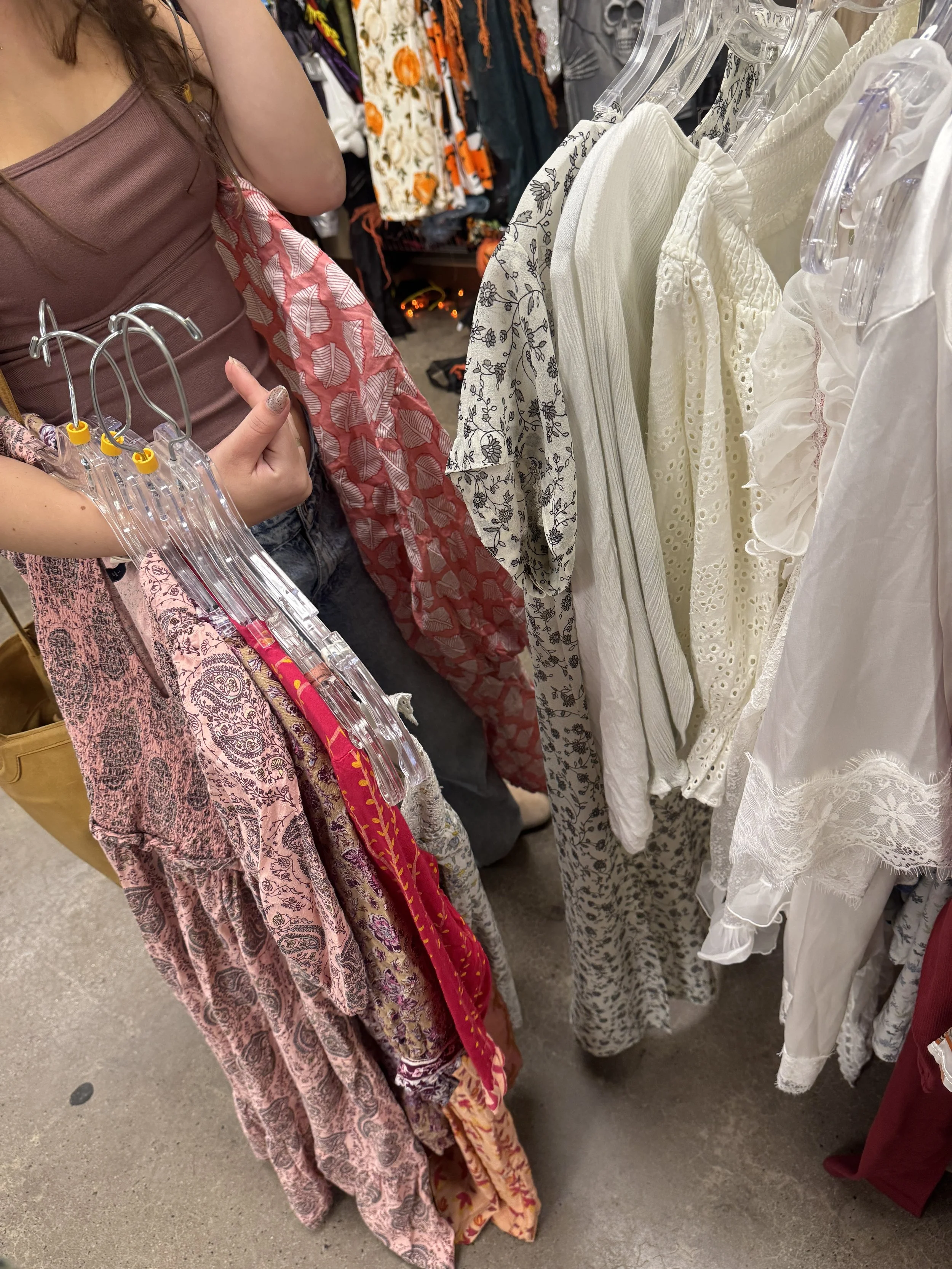 View of a clothing rack with white and cream-colored dresses, along with a woman browsing that is partially visible on the left side of the image.