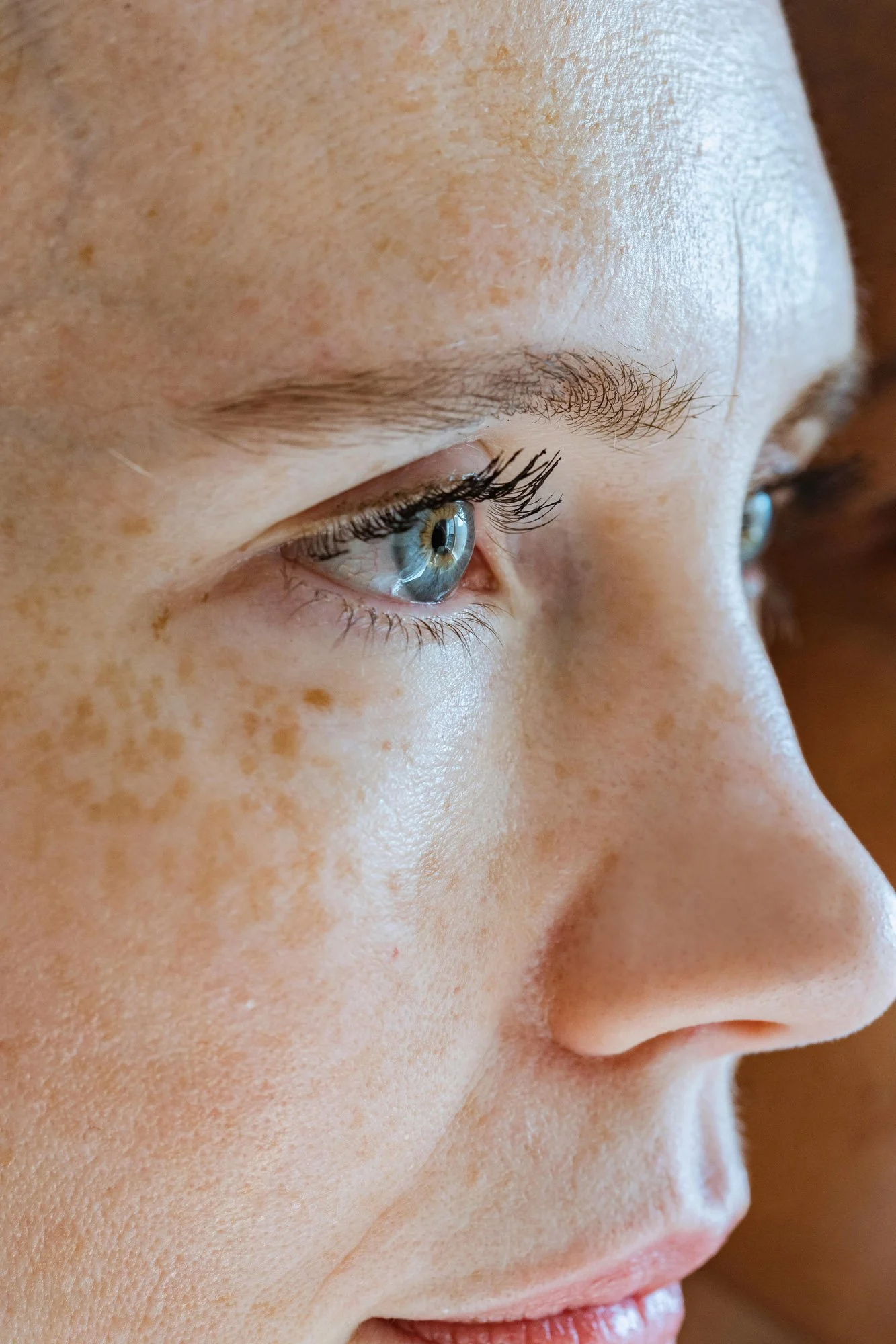Gros plan du visage d'une femme avec un regard vers le bas, mettant en évidence ses yeux, ses sourcils et sa peau claire avec des taches de rousseur.