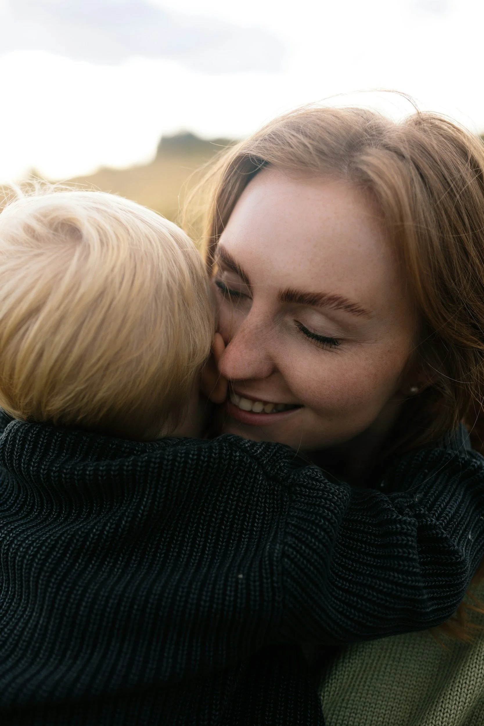 A woman and a young child hugging, close-up shot capturing their faces and expressions of affection.