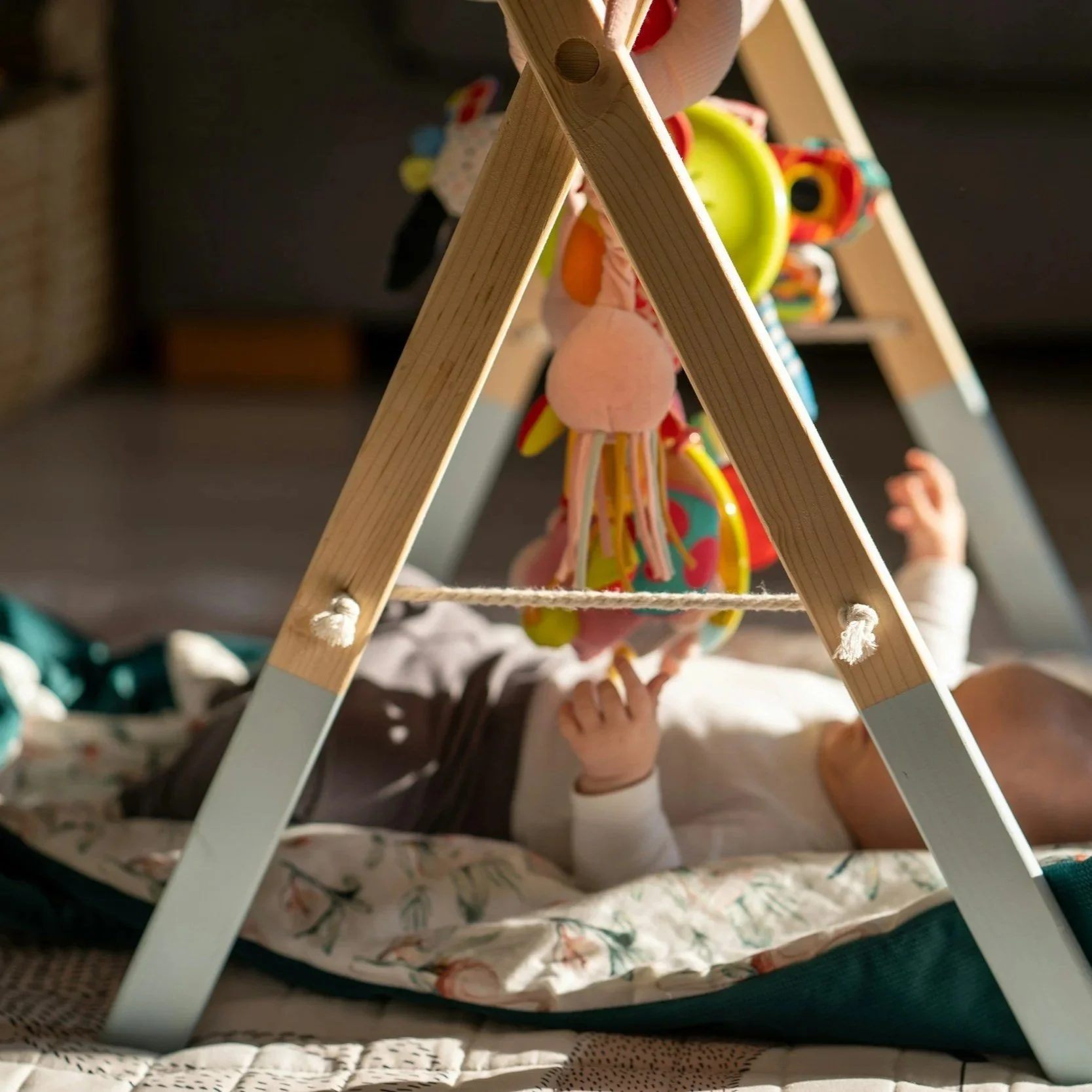 Child holding a colorful stuffed toy beneath a wooden ladder in a cozy room.