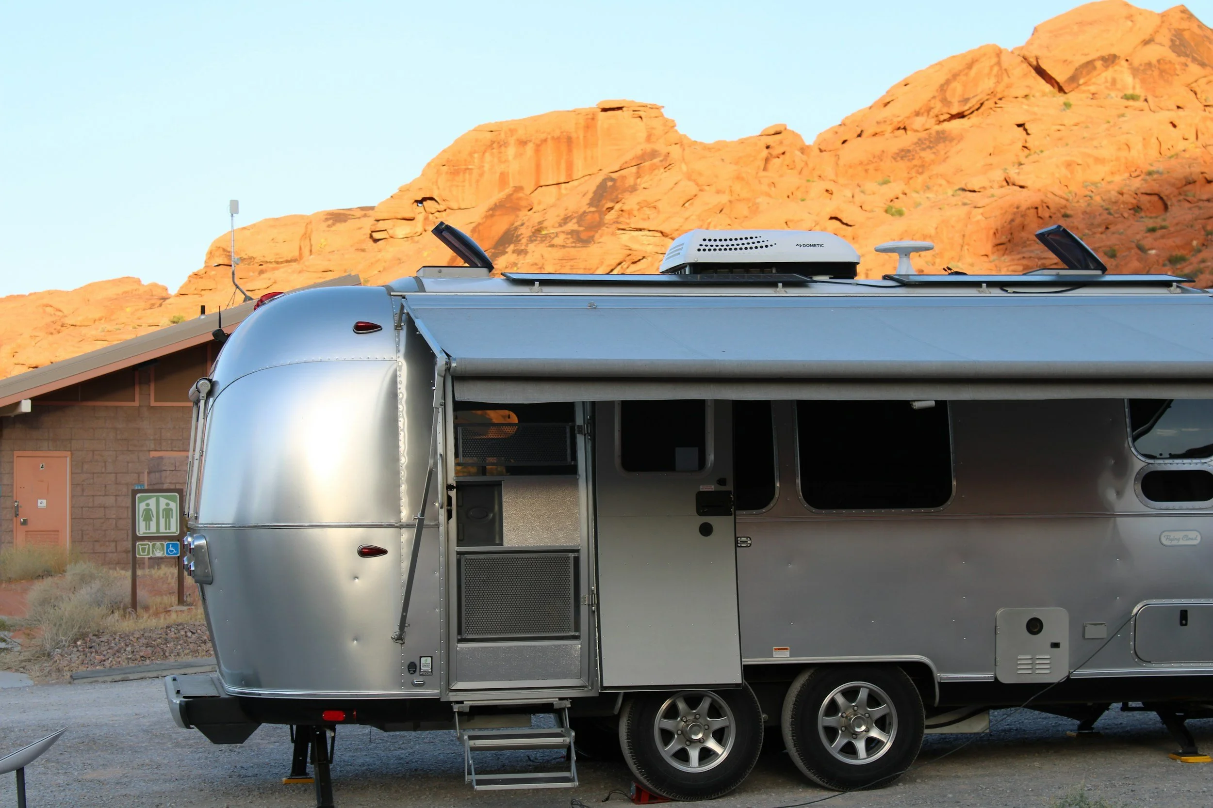 A silver travel trailer parked in front of a desert rock formation at sunset.