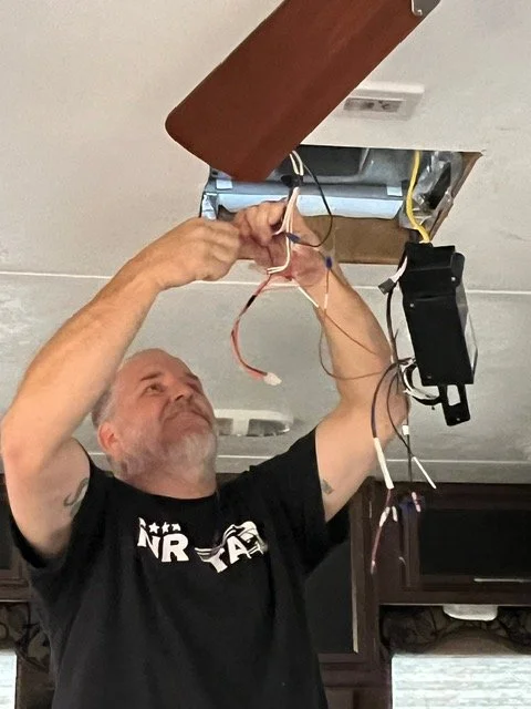 Man installing or repairing electrical wiring in ceiling with tools and wires.