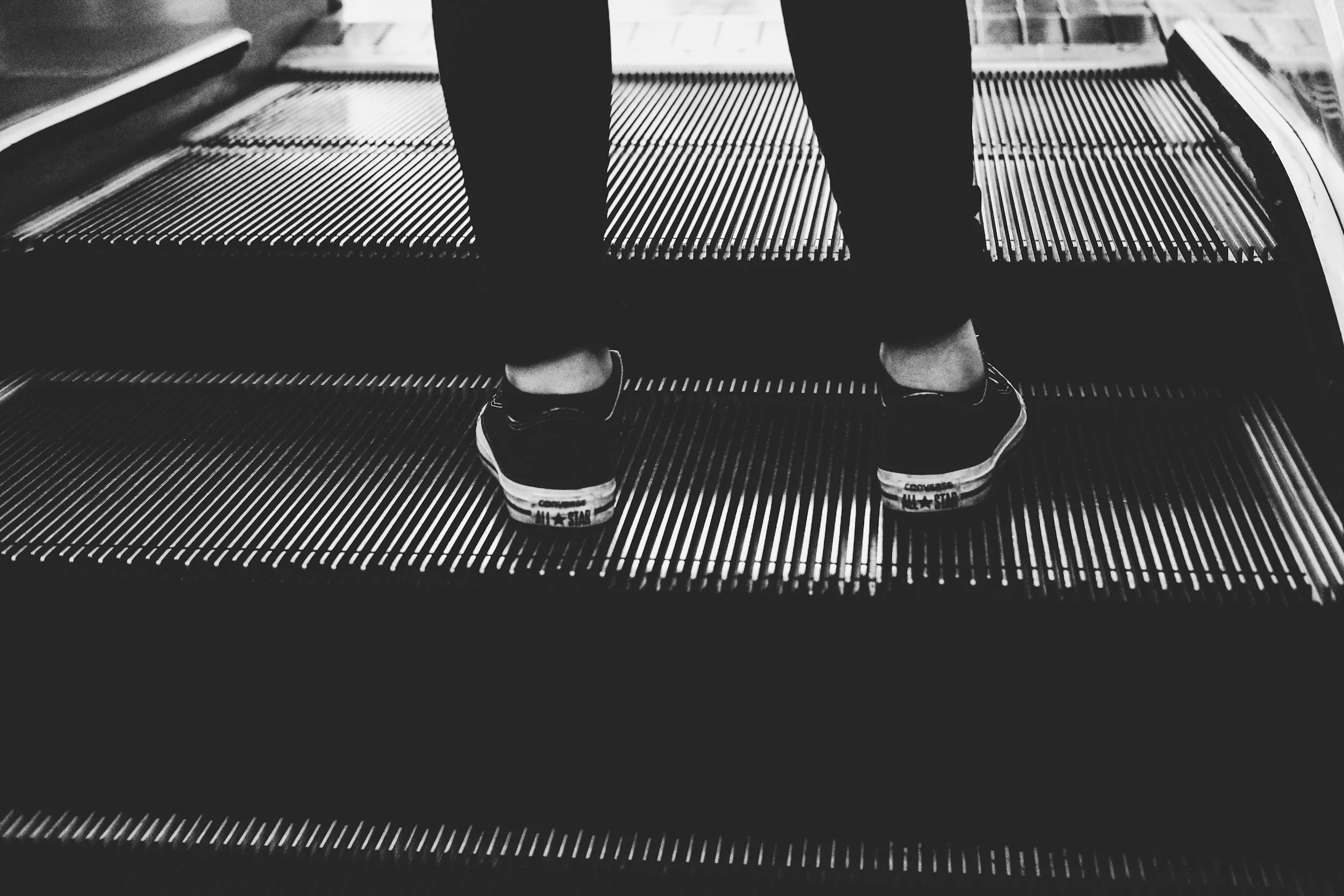 A person stands at the top of an escalator, though only their shoes and lower part of their calves are visible.