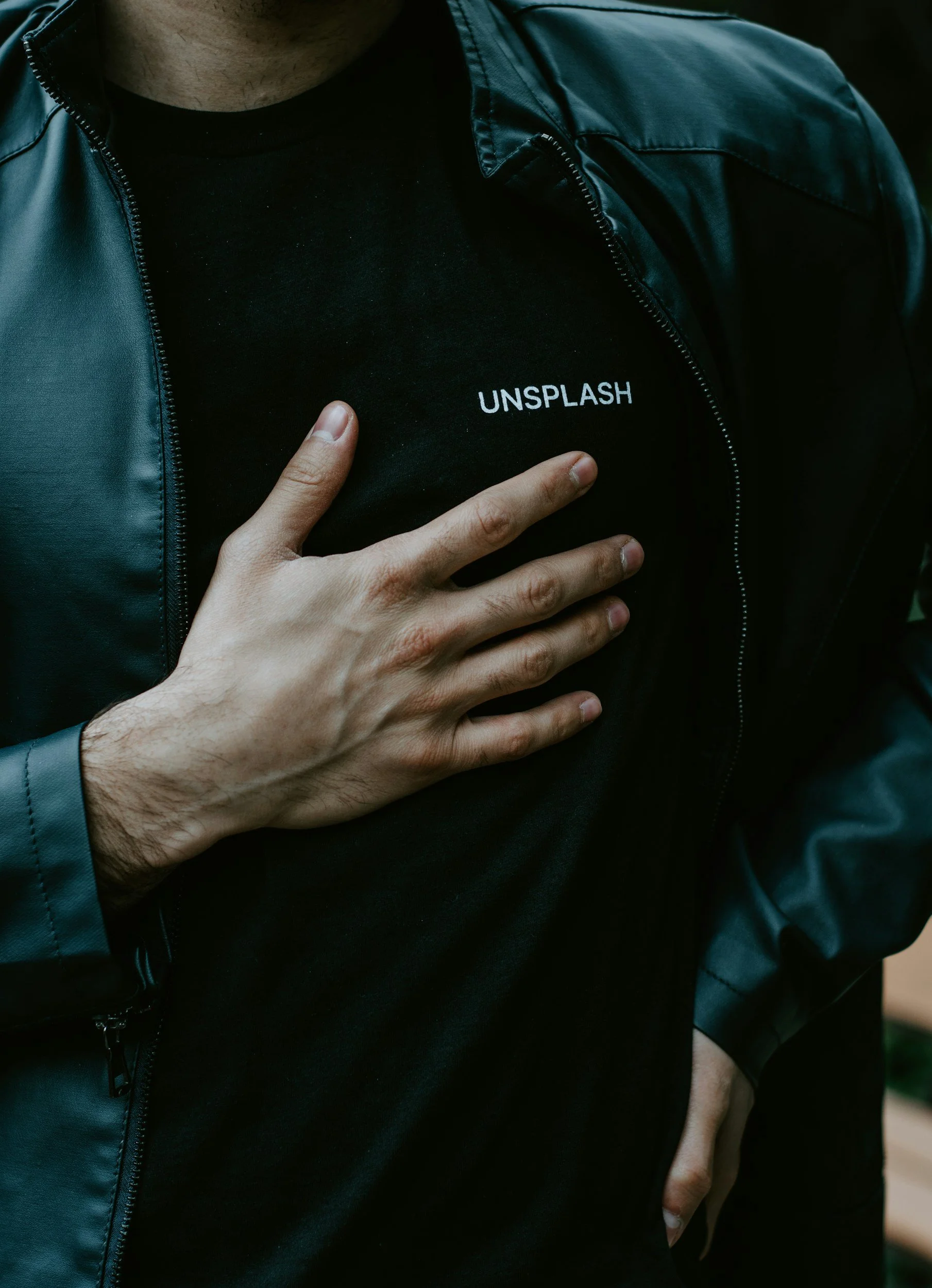 A person holds a hand to their chest. Only their hand and chest are visible. They are wearing a button down shirt with a black shirt underneath.