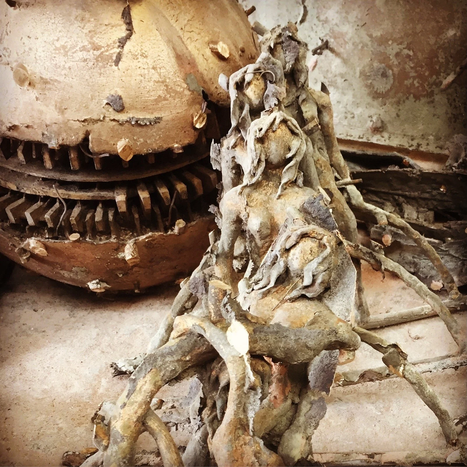 Vertice di una scultura in pietra raffigurante una figura umana, circondata da elementi astratti, con un grande cerchio di metallo arrugginito dietro.