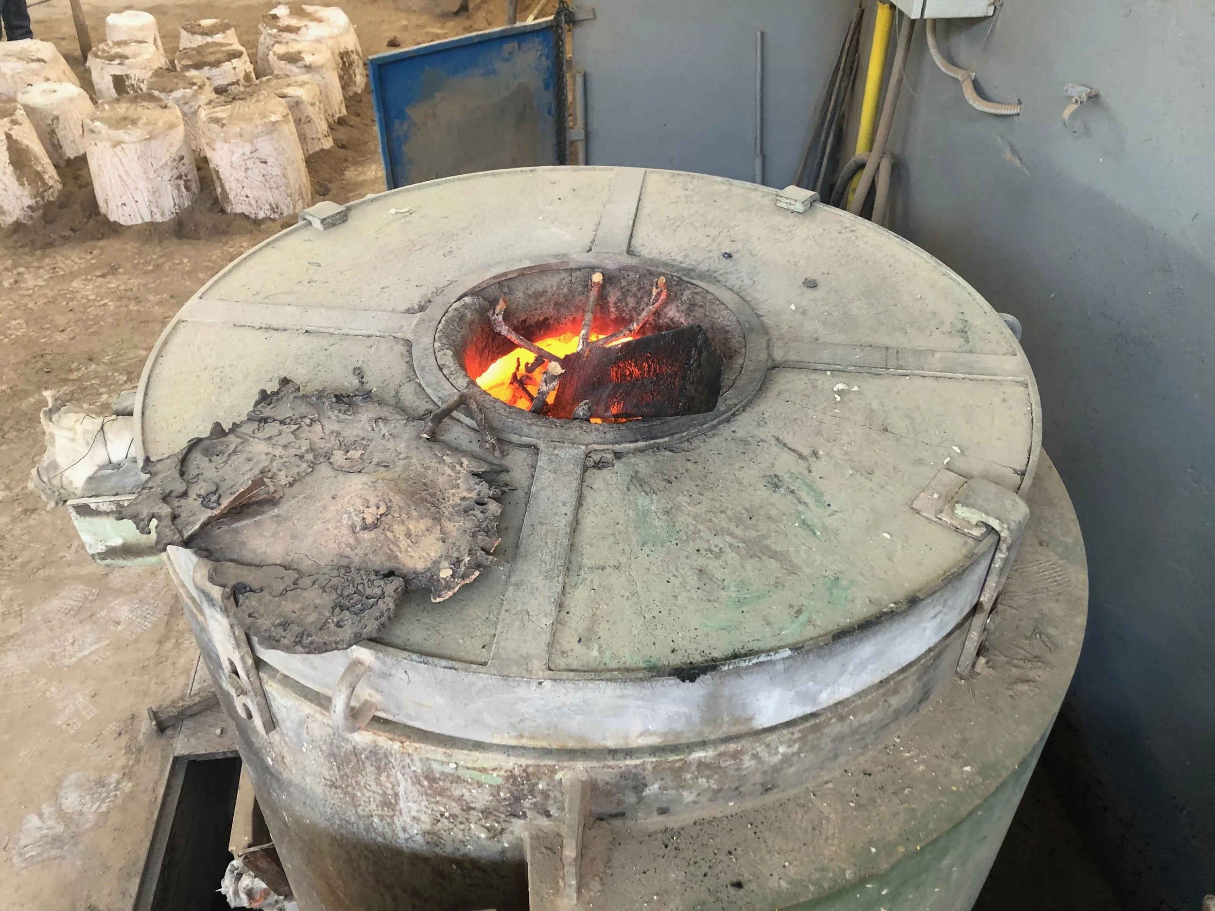 Fornace di altissima temperatura con carbone ardente, circondata da utensili e mattoni in un ambiente di laboratorio o settore industriale.