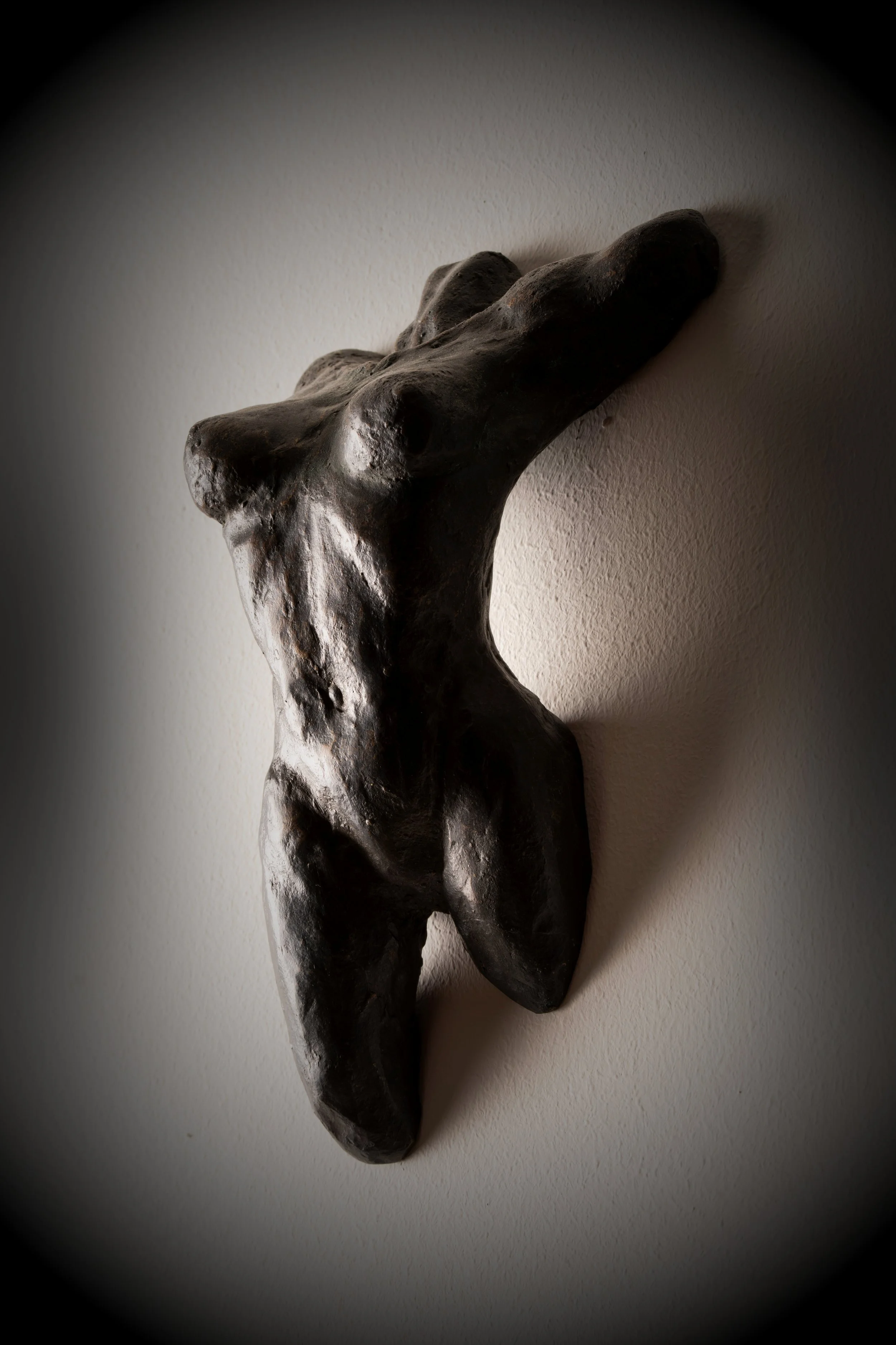 Scultura di un torso umano nudo in stile astratto, in bronzo, appoggiata a parete.