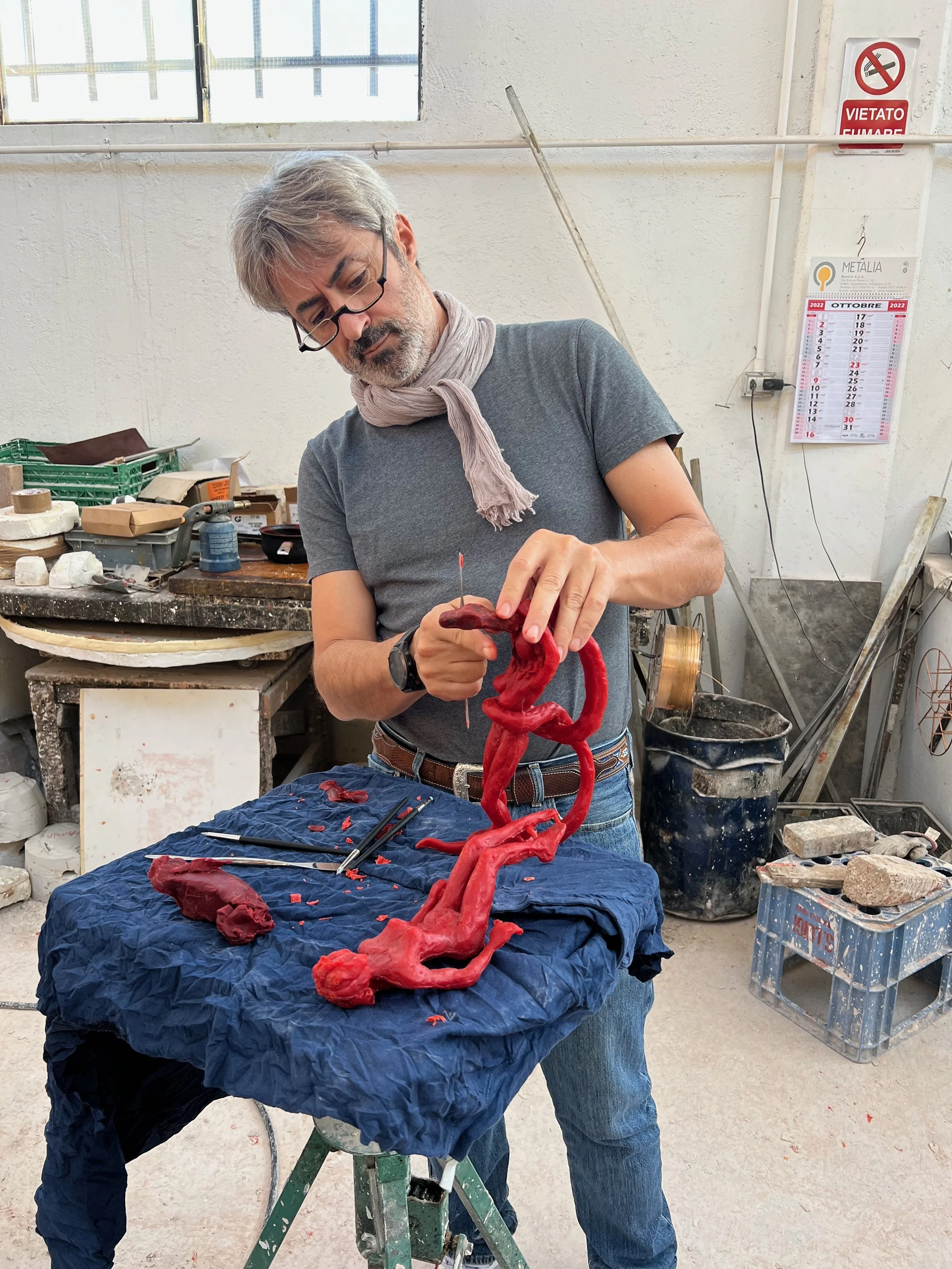 Un artista sta scolpendo una figura umana in argilla rossa su un tavolo di lavoro in un laboratorio.