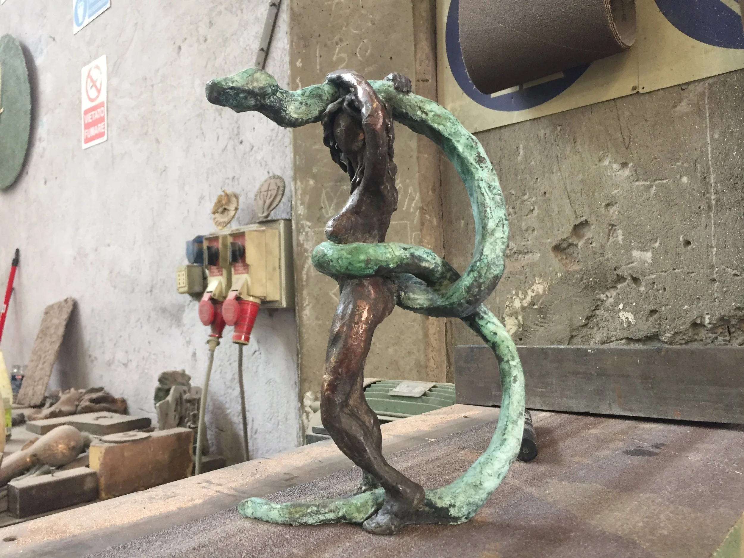 Scultura in metallo con forme curve e organiche in ambiente di officina o studio di lavorazione dei metalli.