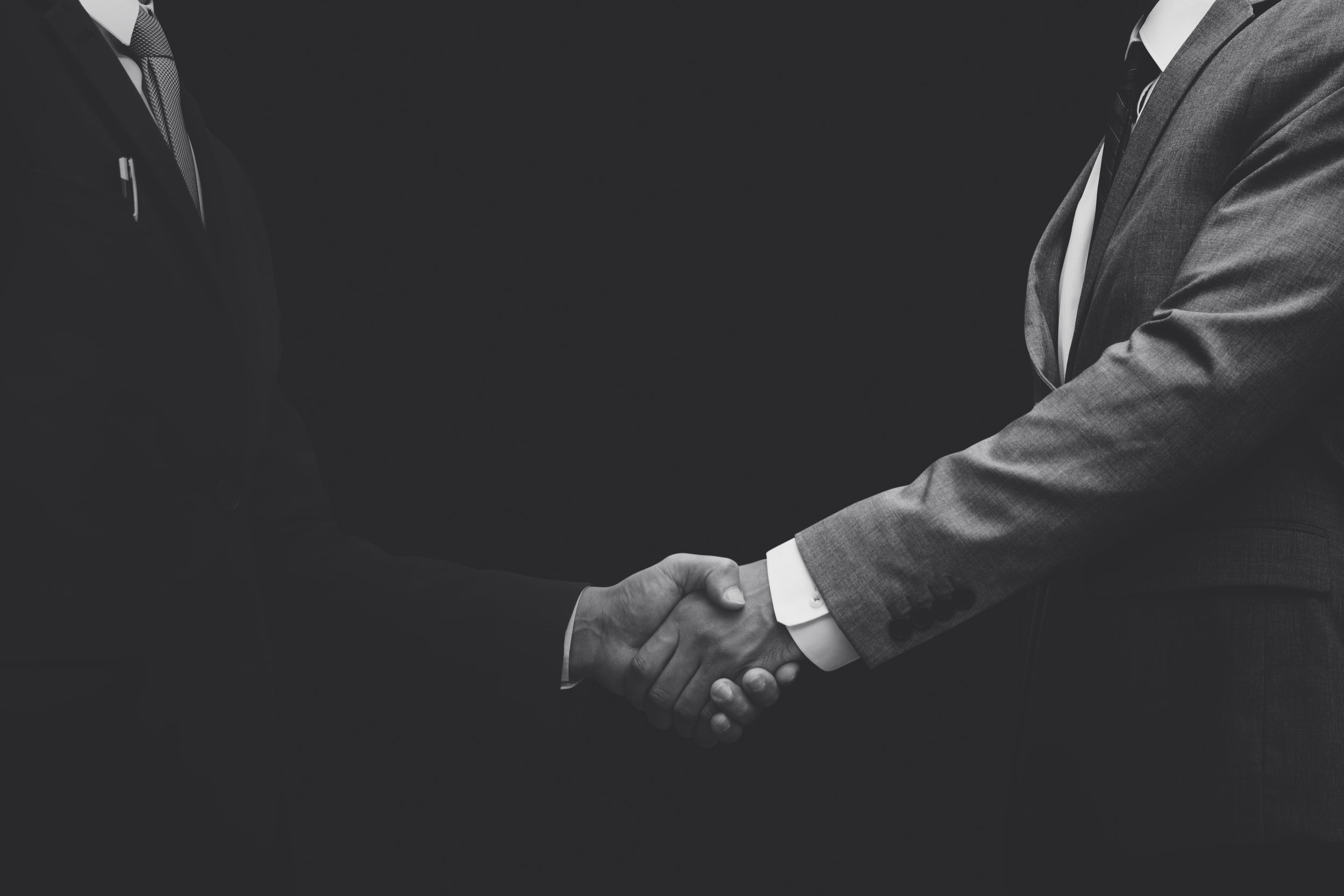 Two people in suits shaking hands against a dark background.