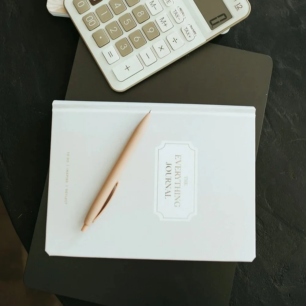 A notebook, pen and calculator on a dark desk