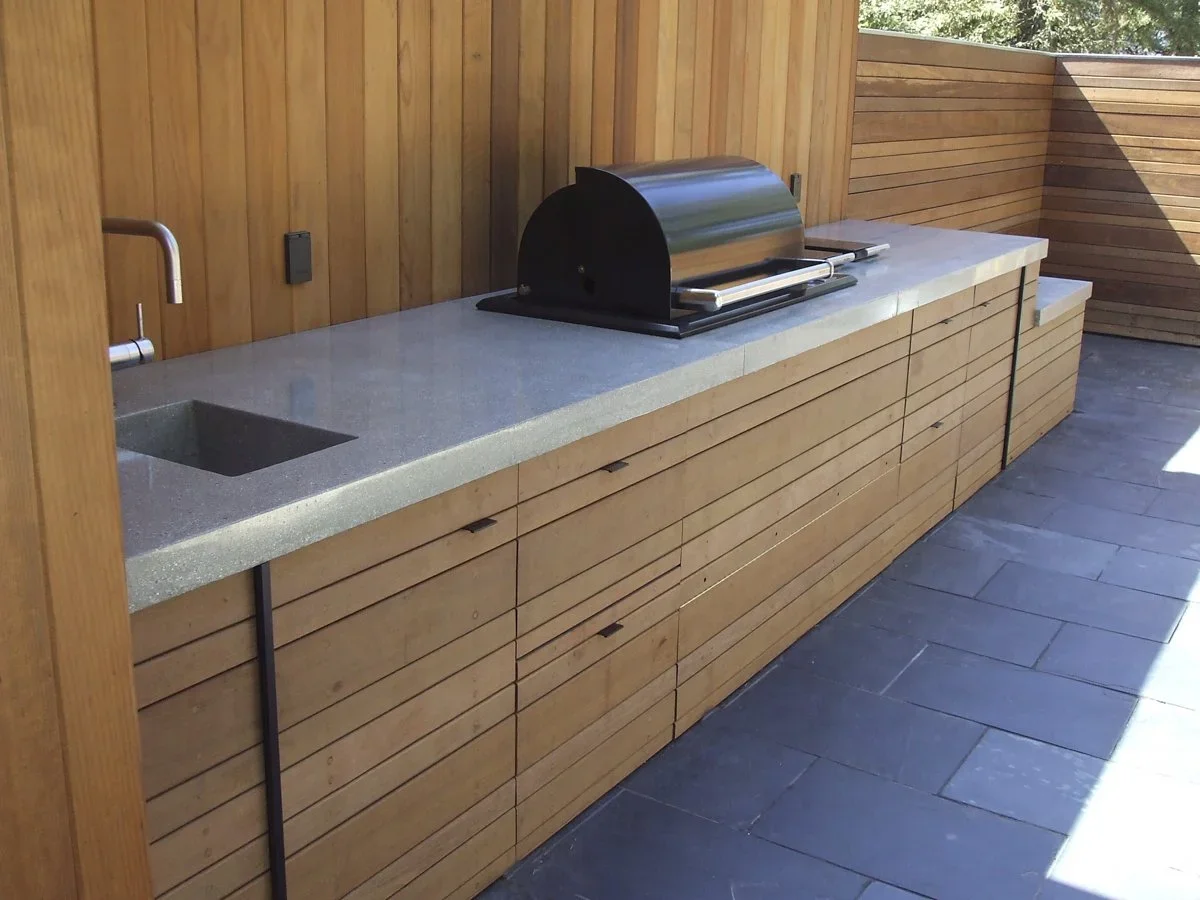 Outdoor kitchen with a built-in grill, sink, and wooden cabinetry on a balcony or patio.