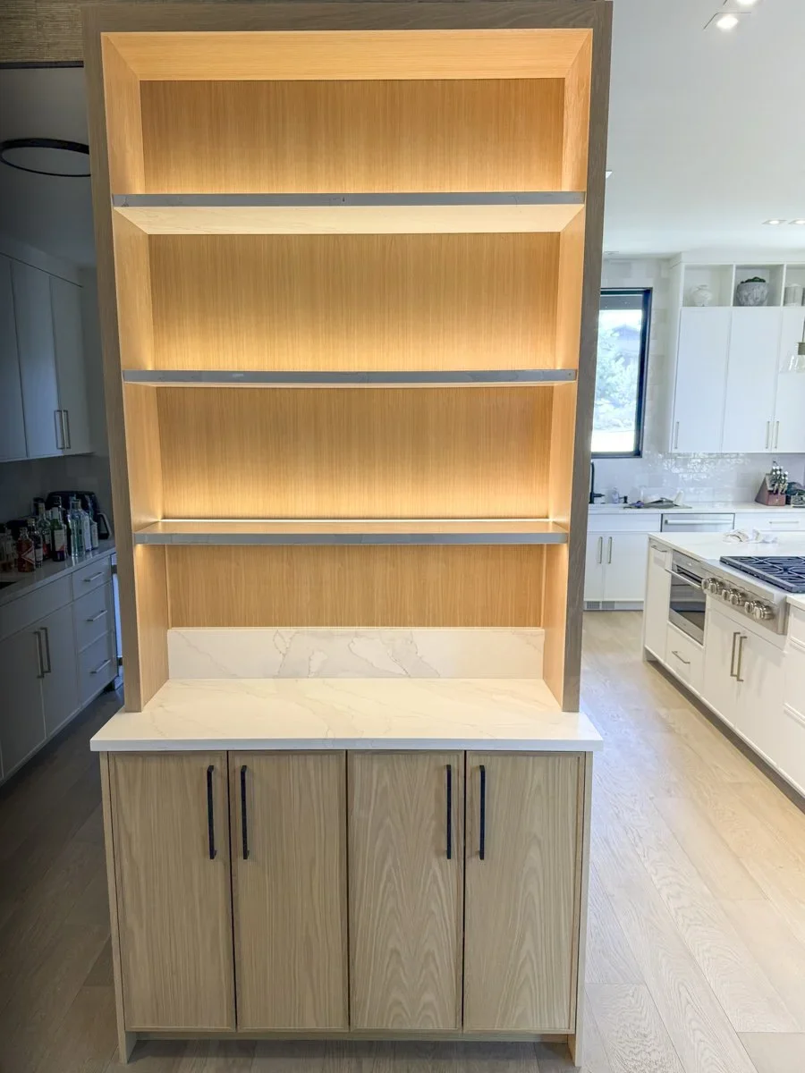 A wooden kitchen bookshelf with four open shelves and a marble countertop at the bottom, located in a modern kitchen.
