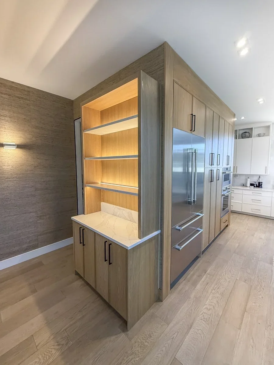 Modern kitchen with wooden cabinets, built-in shelves, stainless steel appliances, and light-colored hardwood flooring.