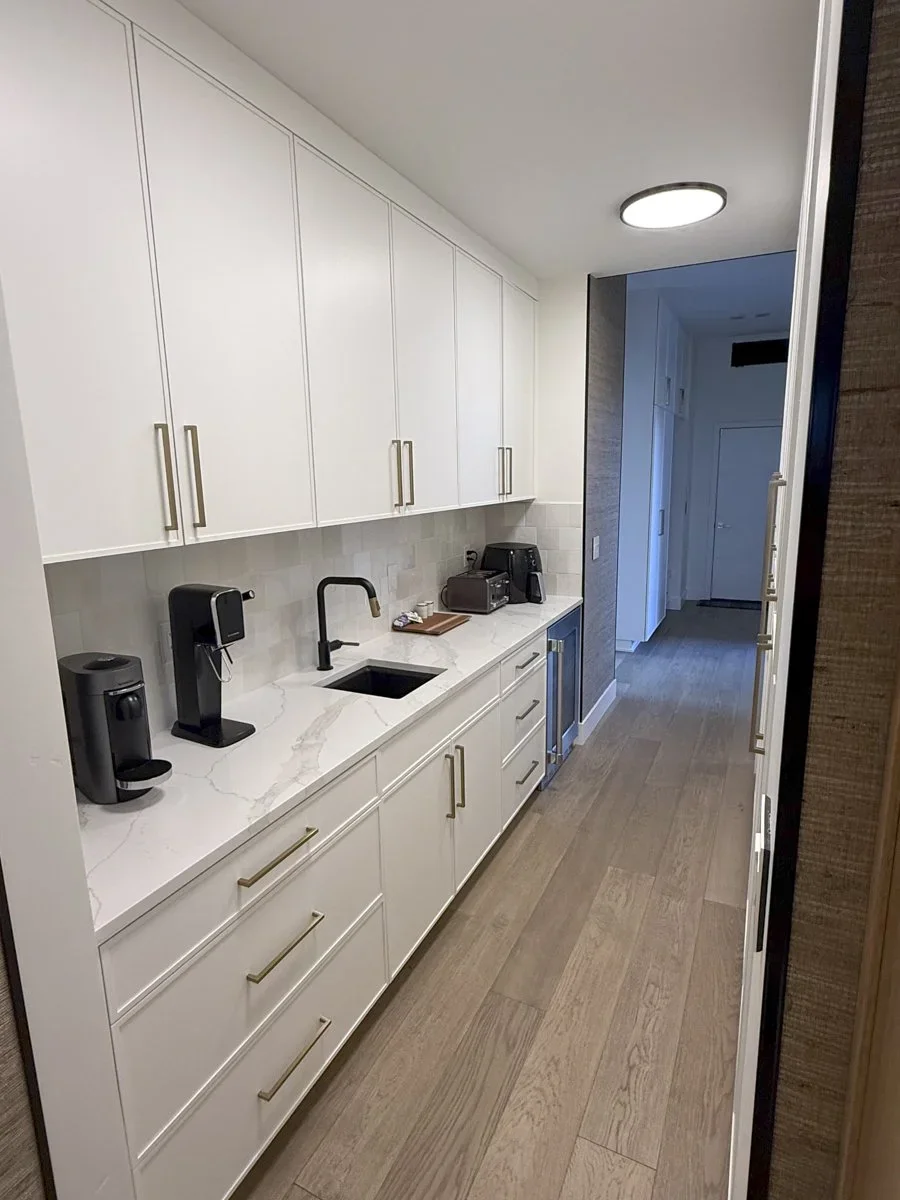 Modern kitchen with white cabinets, marble countertop, small sink, coffee maker, toaster, microwave, and other small appliances, with wood flooring and ceiling lighting.