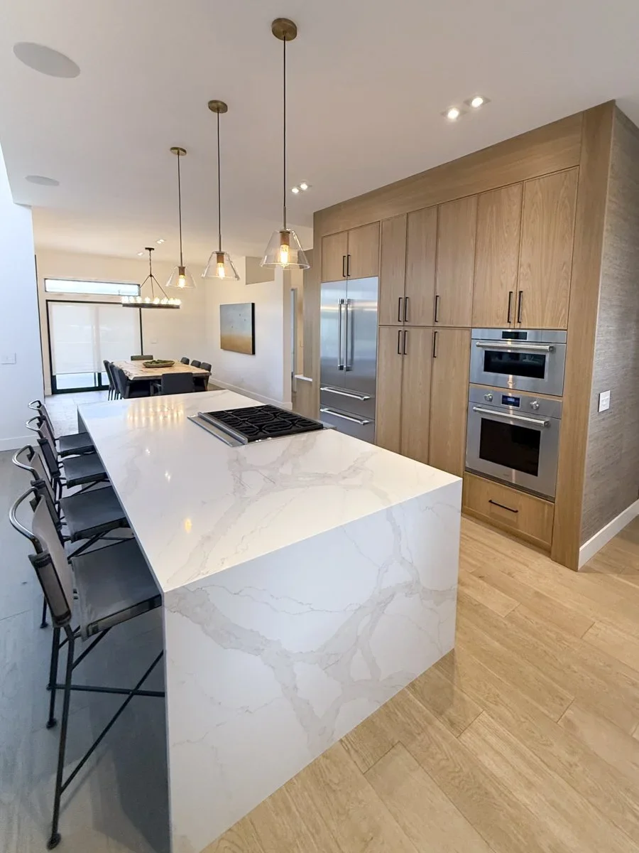 Modern kitchen with a white marble island, wooden cabinetry, stainless steel appliances, and pendant lights.