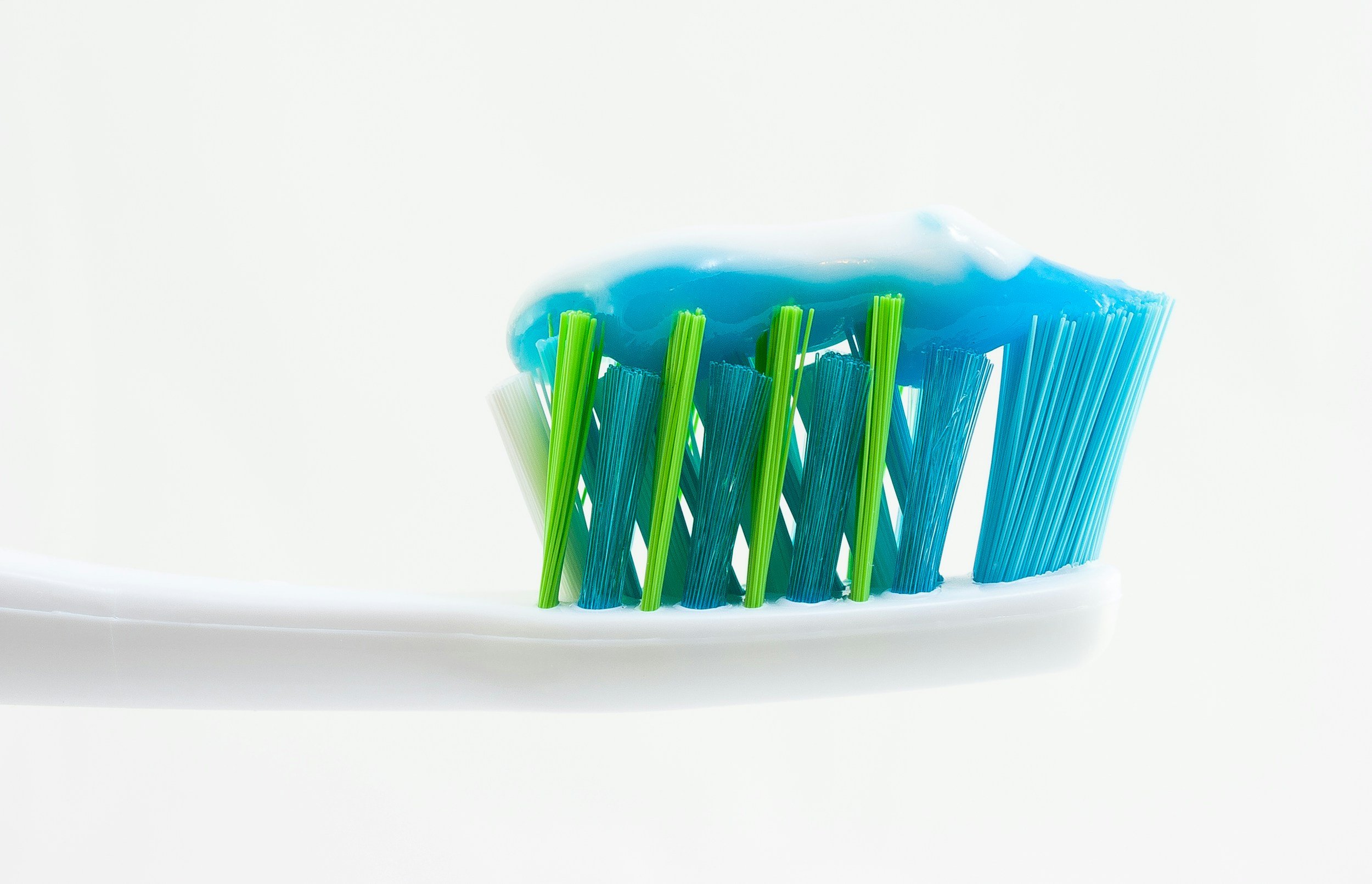 Close-up of a toothbrush with blue and green bristles and white toothpaste on top against a white background.