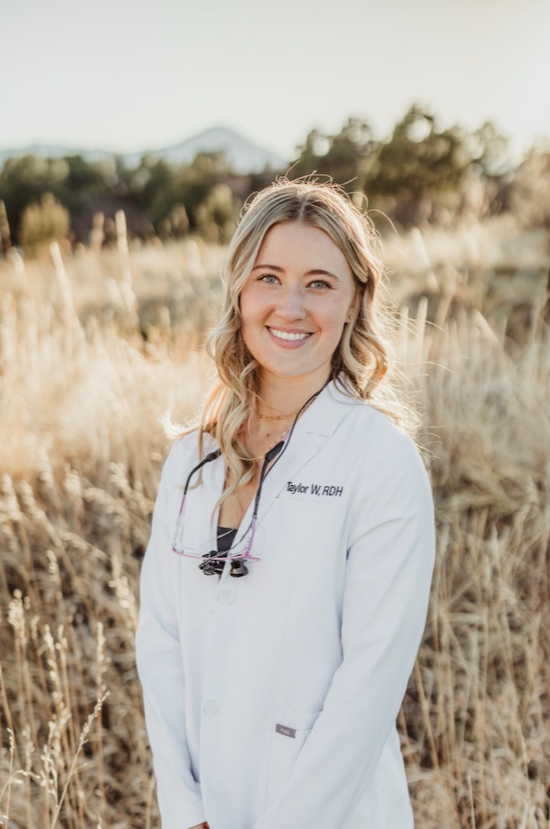 A young woman in a white medical coat smiling outdoors in a field during sunset.