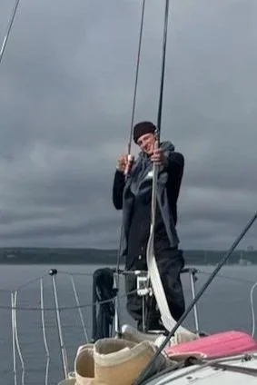 Person on a sailboat pointing at the camera during cloudy weather.