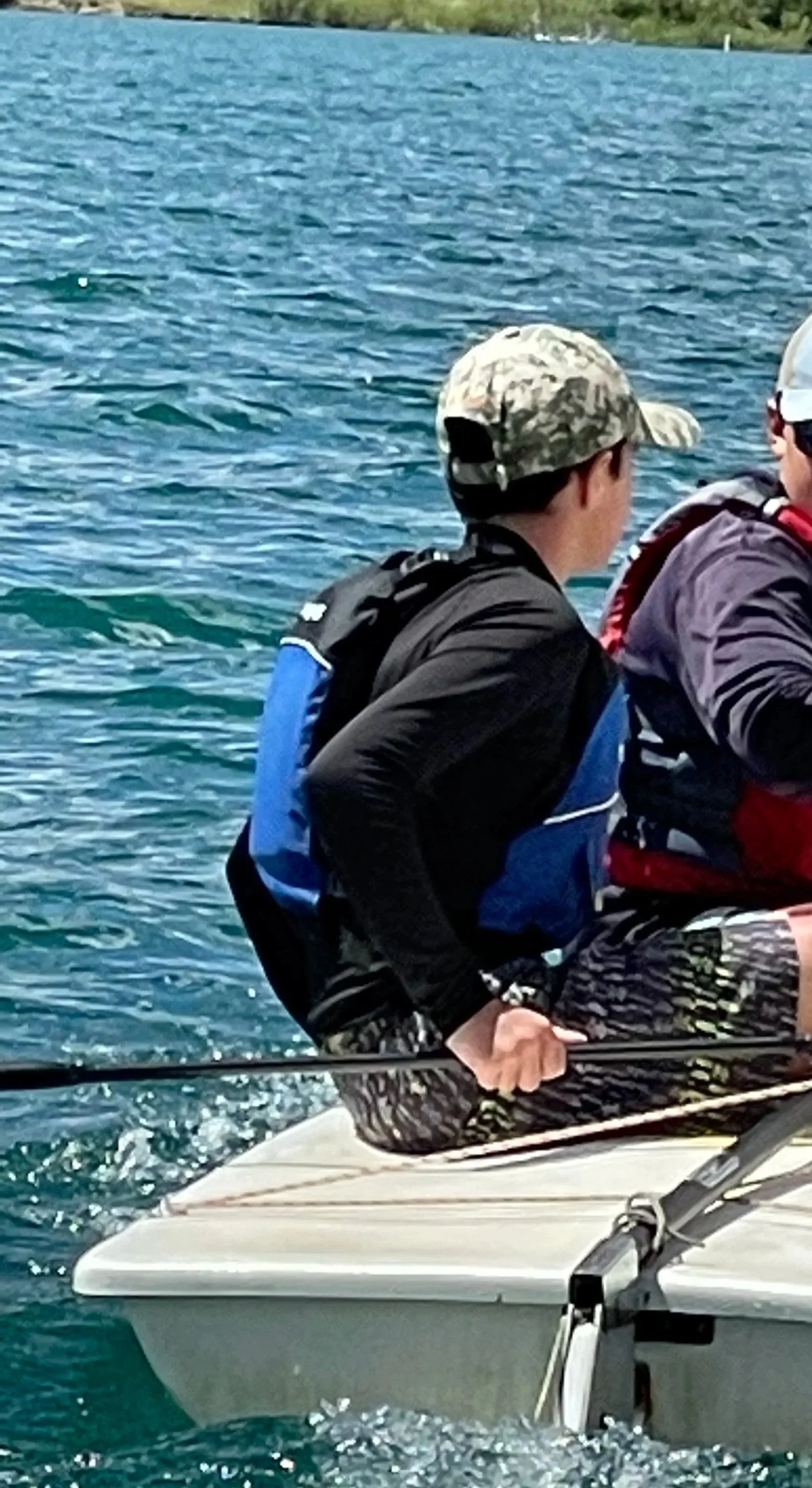 Two people sitting on a small boat with a person in the middle holding a fishing rod, on a body of water.