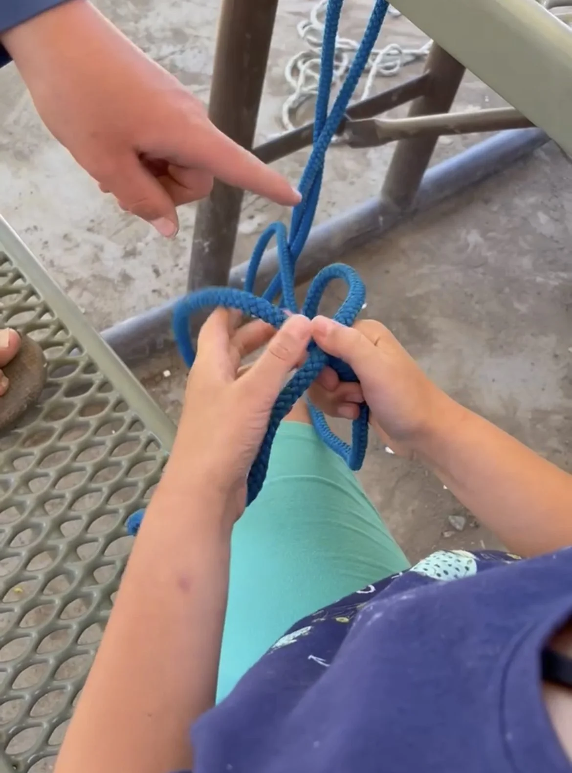 Person tying a blue rope into a knot while sitting on a bench outdoors.