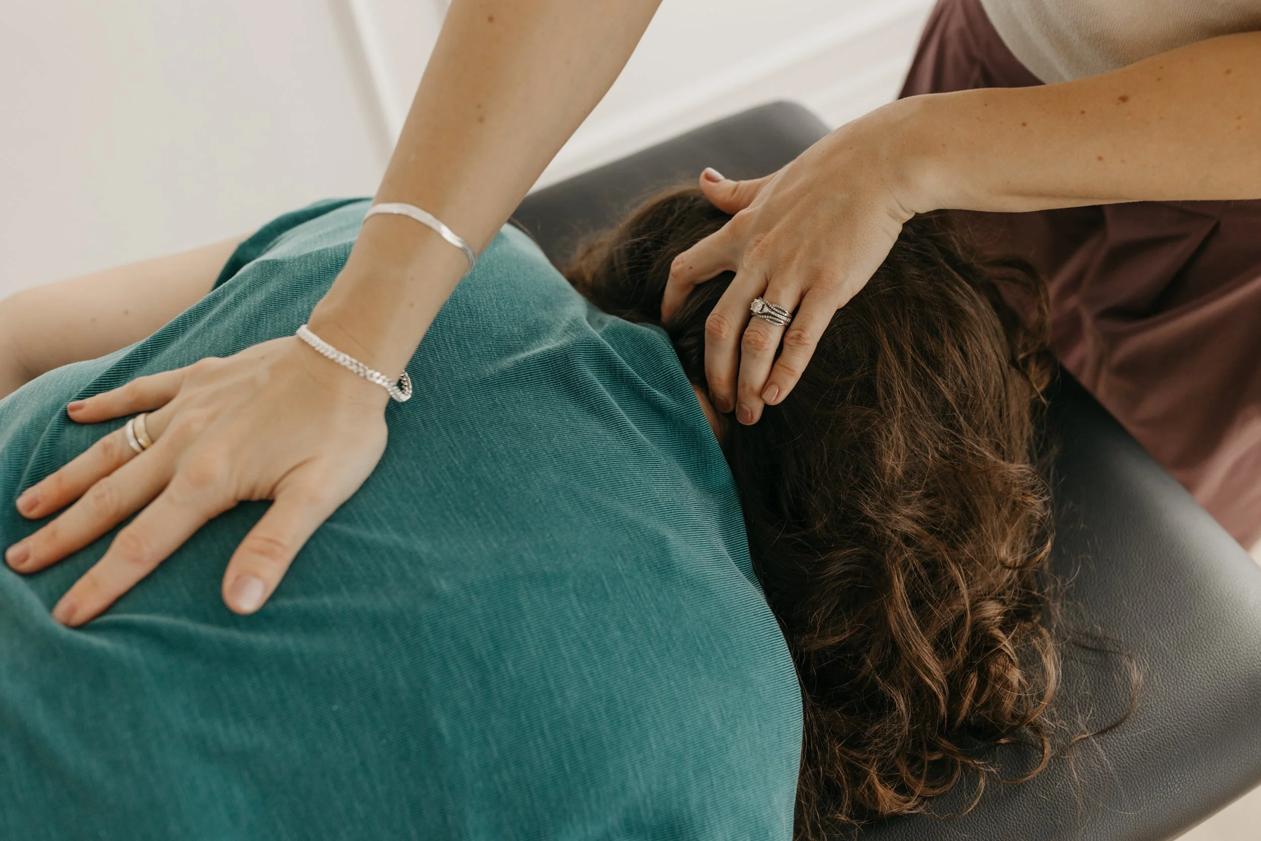 A person receiving a massage, lying face down with their head turned to the side, while another person applies pressure to their back with their hands.