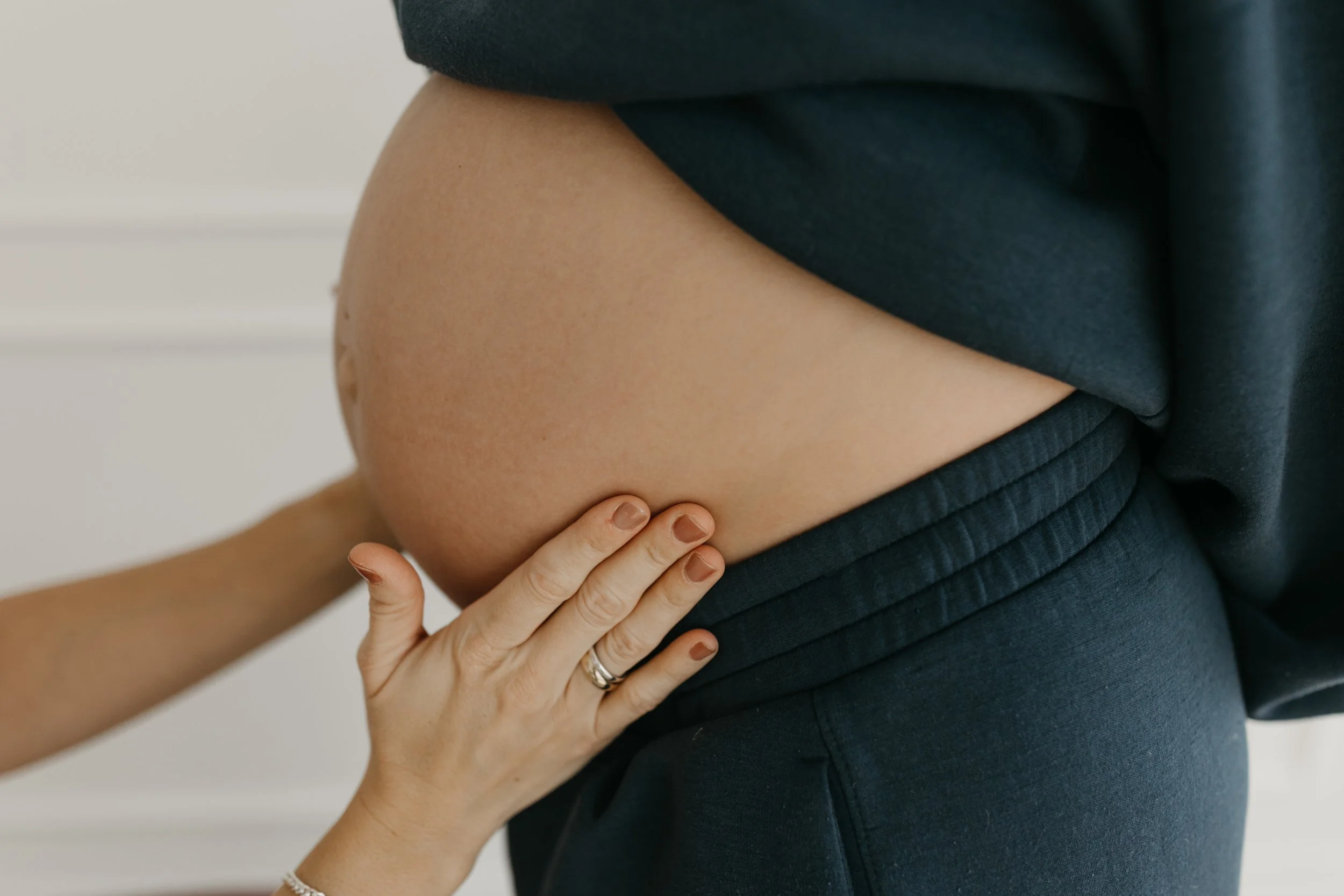 Close-up of a pregnant woman's belly being gently touched by a person with a wedding ring, with the woman wearing black clothing.
