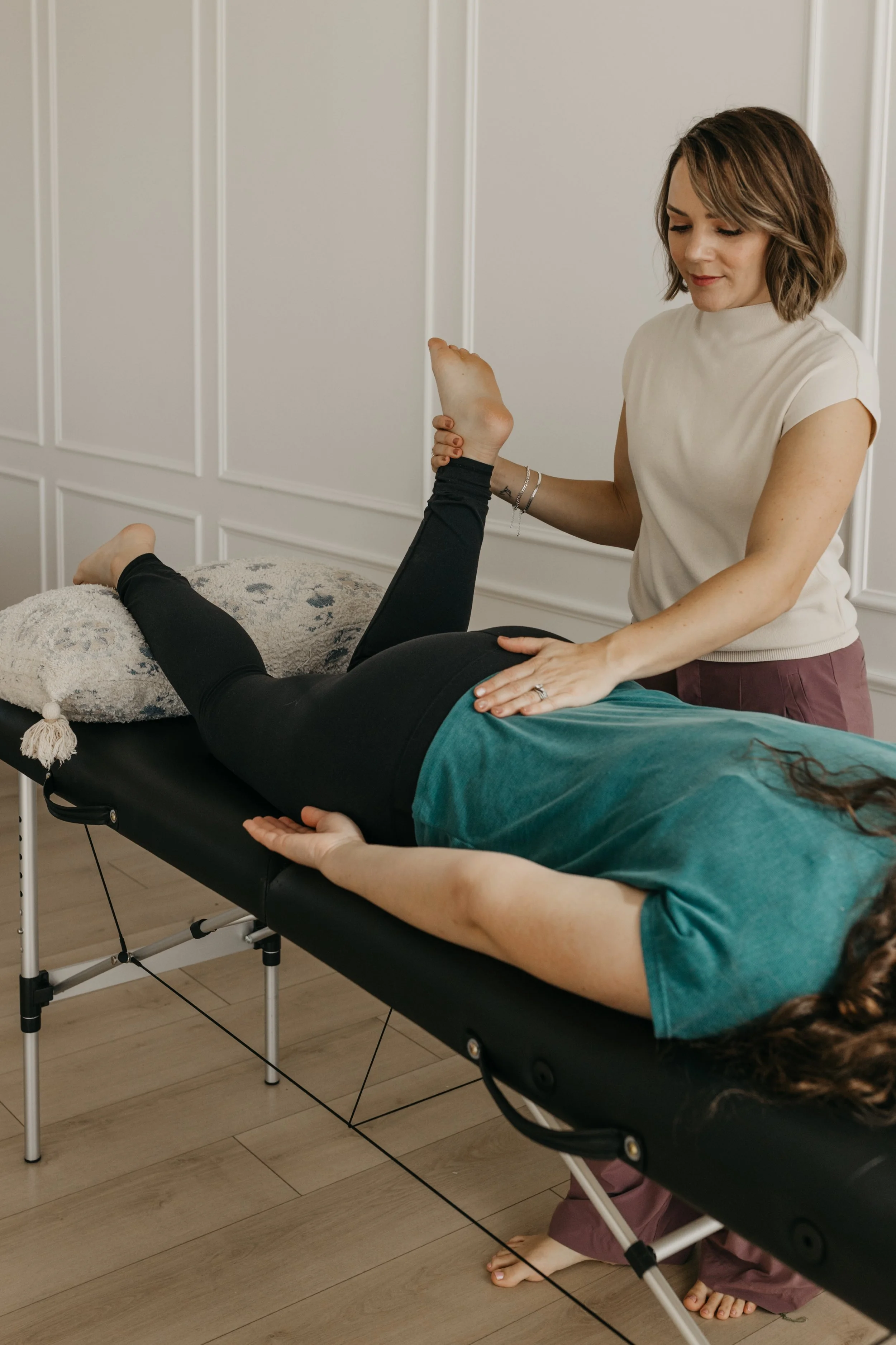A woman receiving a physical therapy or massage on her leg while lying on a treatment table in a therapy room.