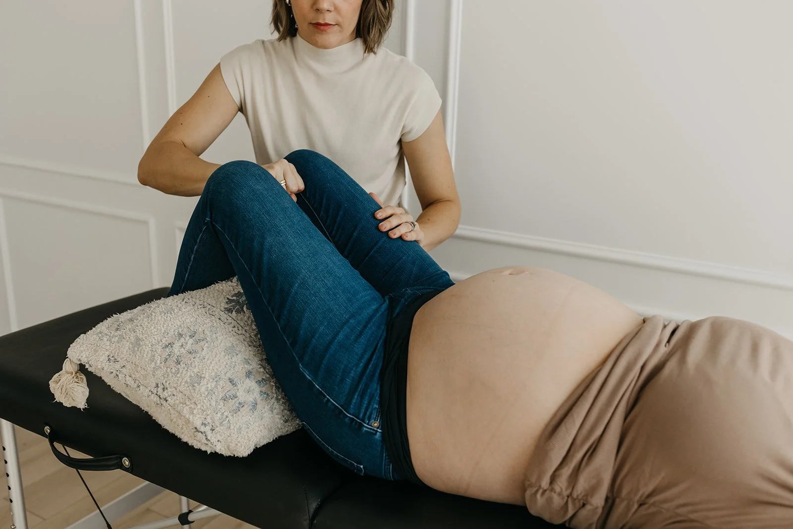Pregnant woman lying on a massage table with her knees bent, receiving a prenatal massage from a therapist.